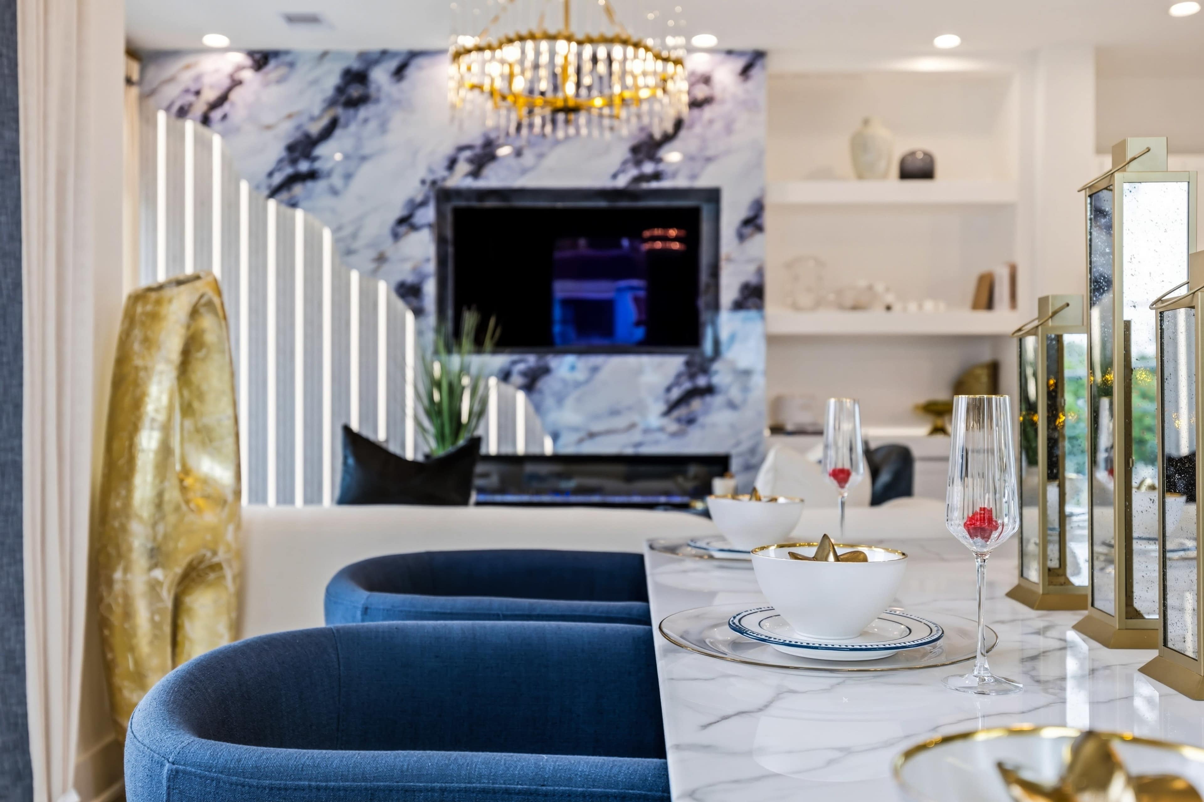 A modern dining area features a marble table set with glassware and decorative bowls, alongside a stylish living space with textured walls and elegant lighting.