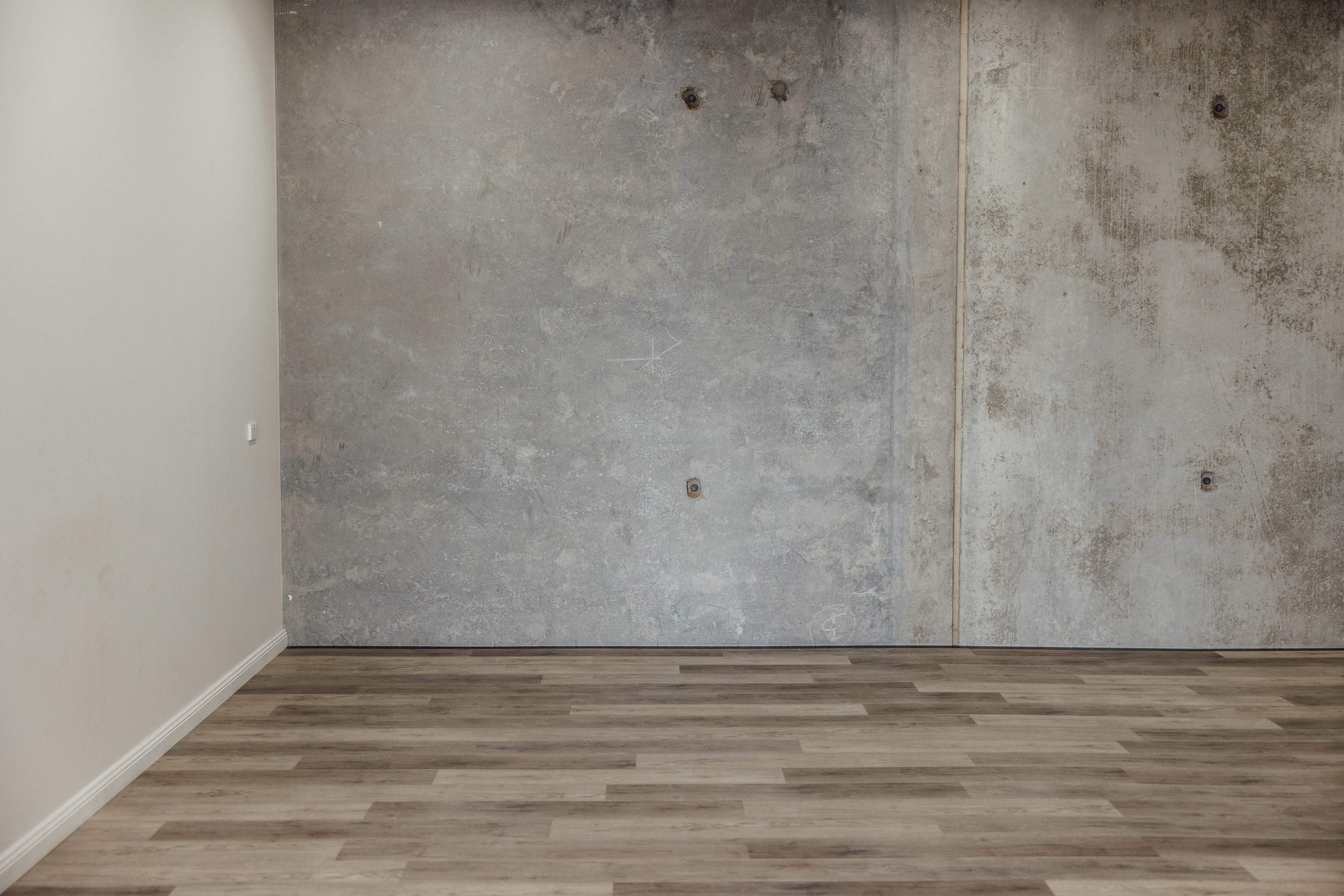 An empty room with a wooden floor and a gray concrete wall.
