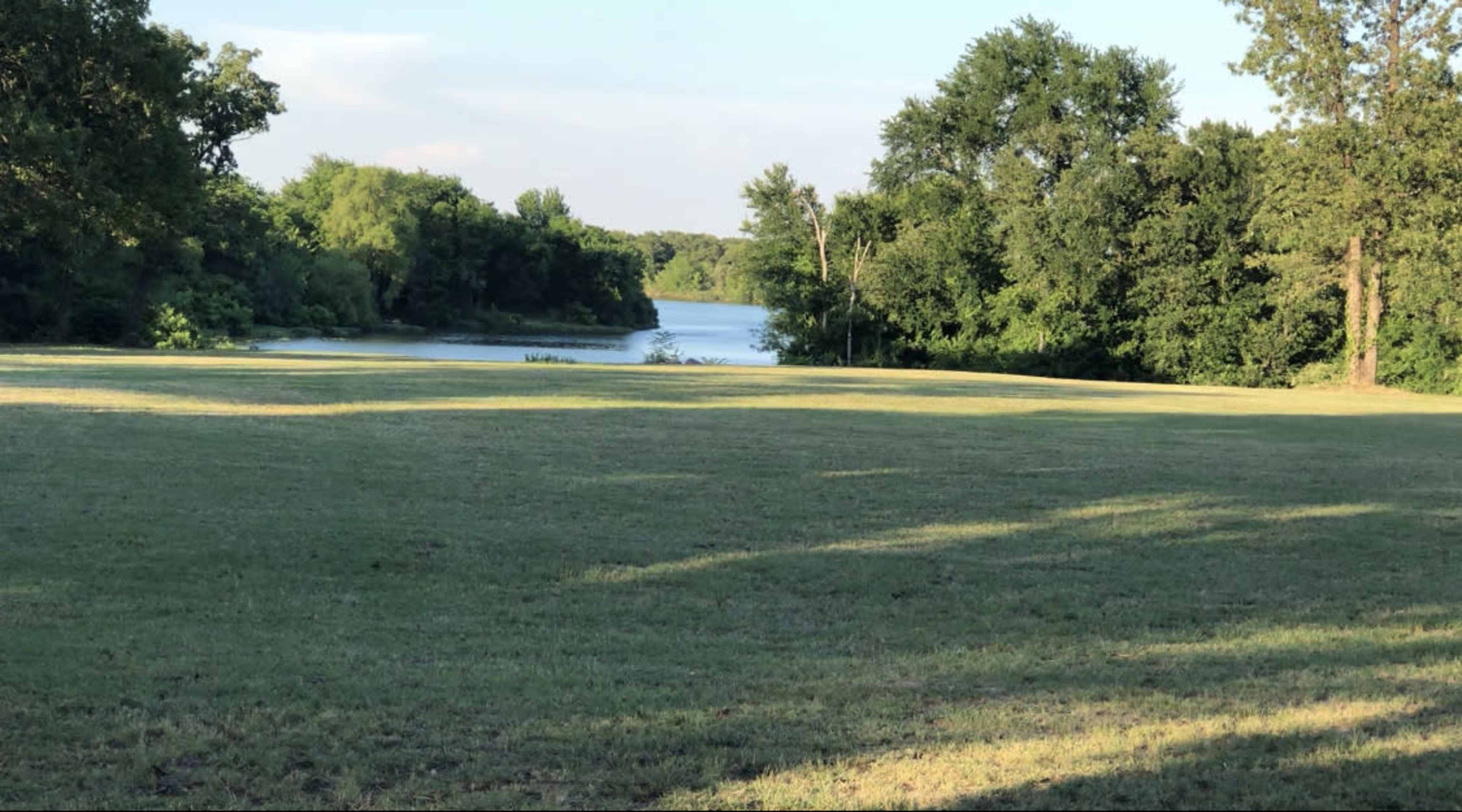 A grassy area sloping down to a calm river bordered by trees.