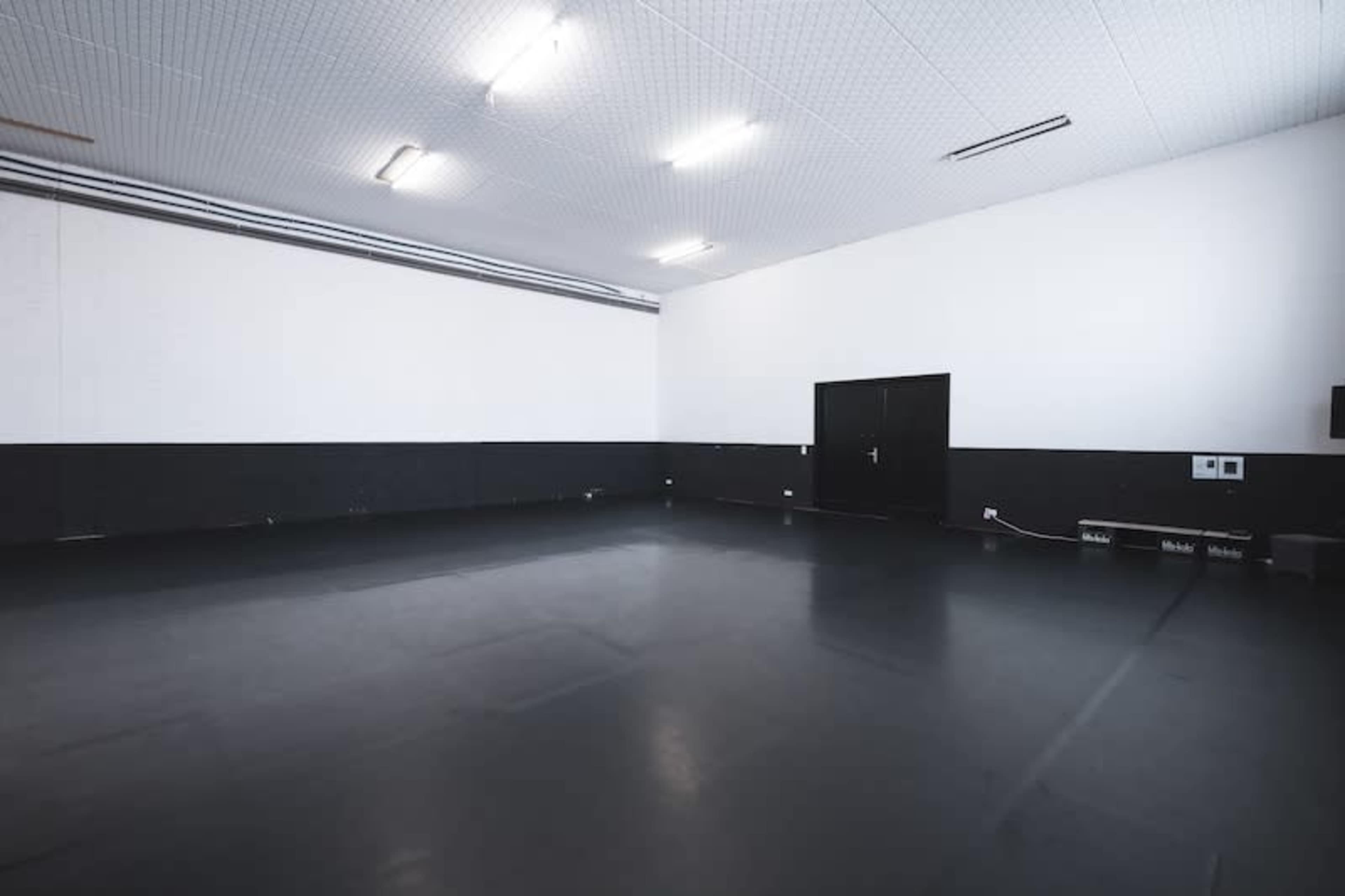A large, empty room with black flooring, white walls, and fluorescent lighting.