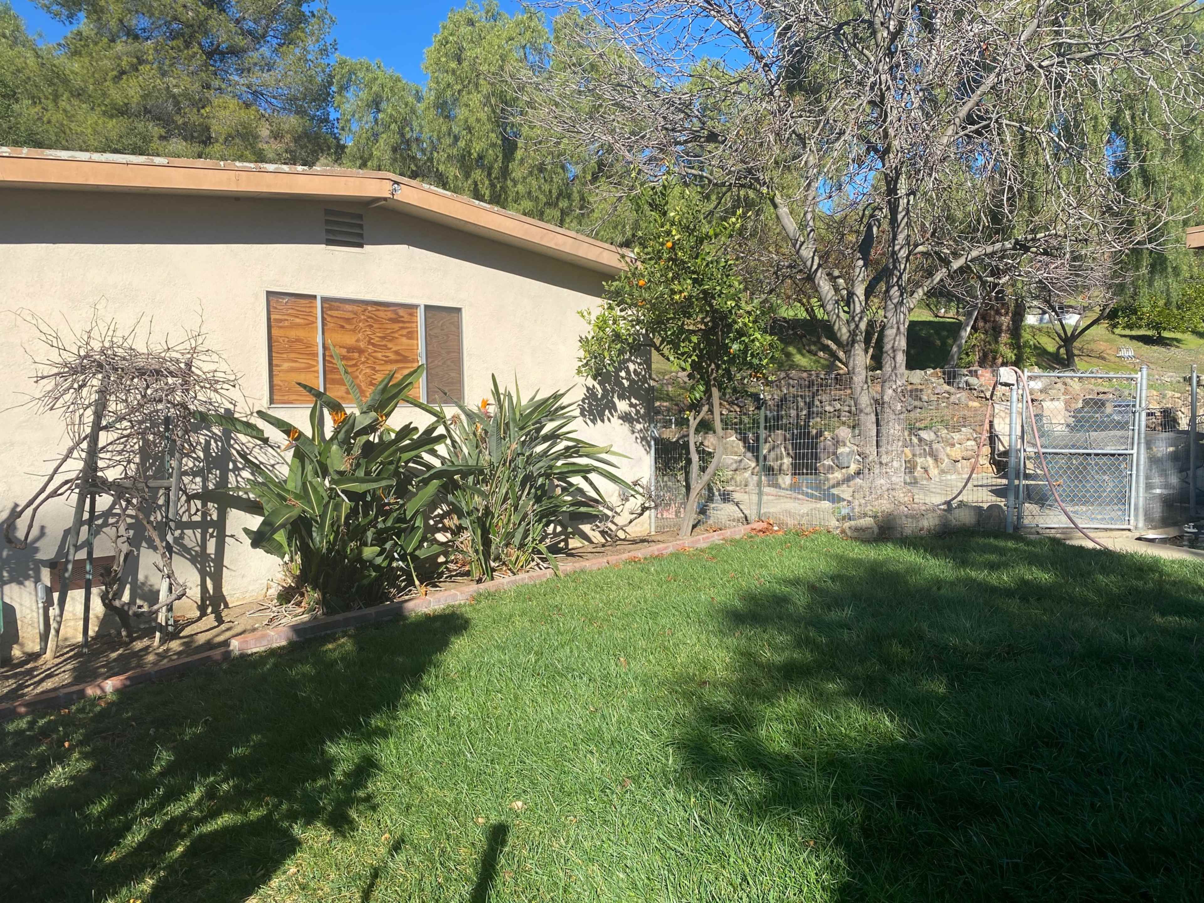 The image shows a backyard with a house, a garden featuring shrubs and plants, and a fenced area with a gate in the background.