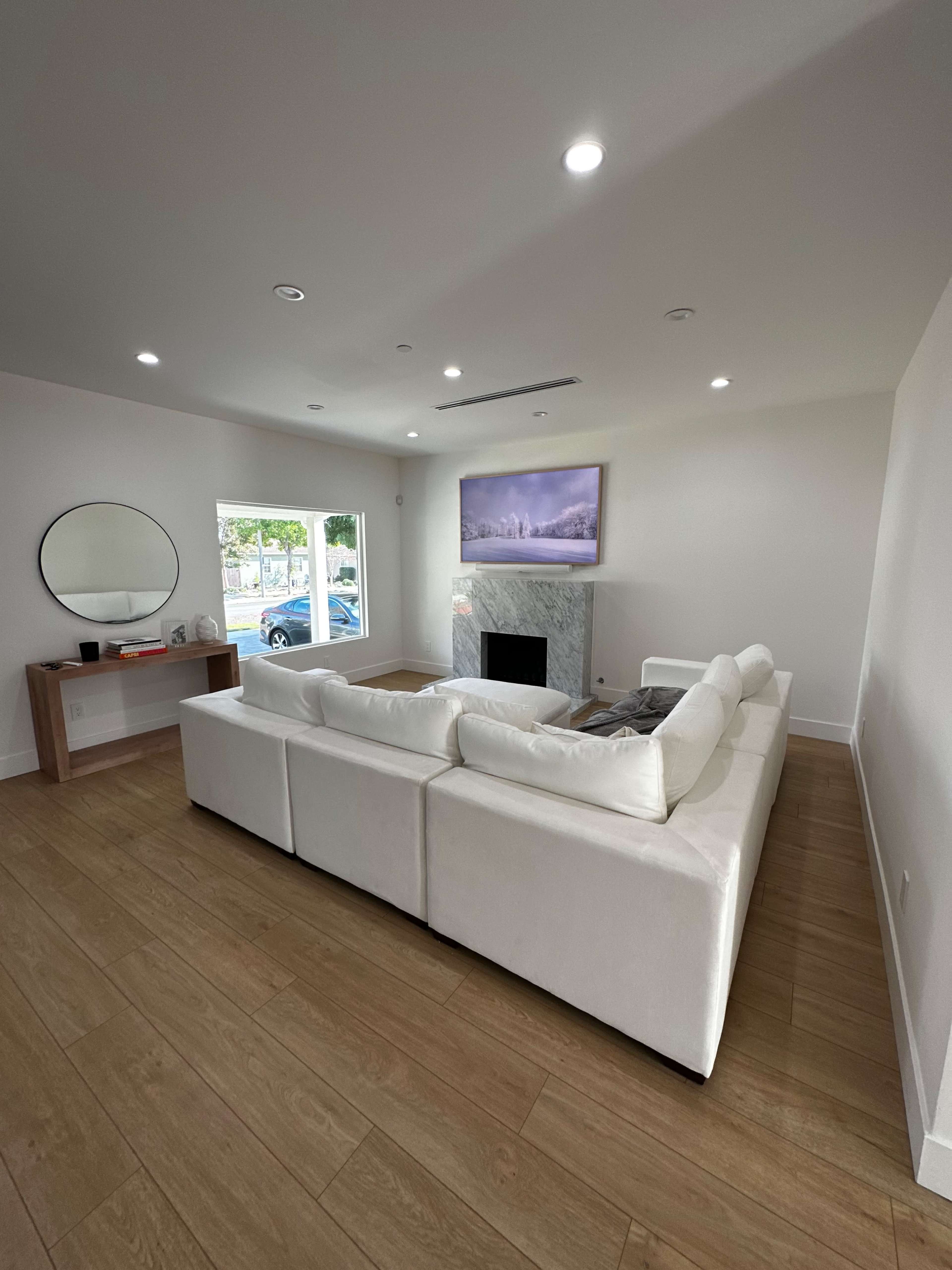 The image shows a modern living room with a white sectional sofa, a marble fireplace, and a wall-mounted television.