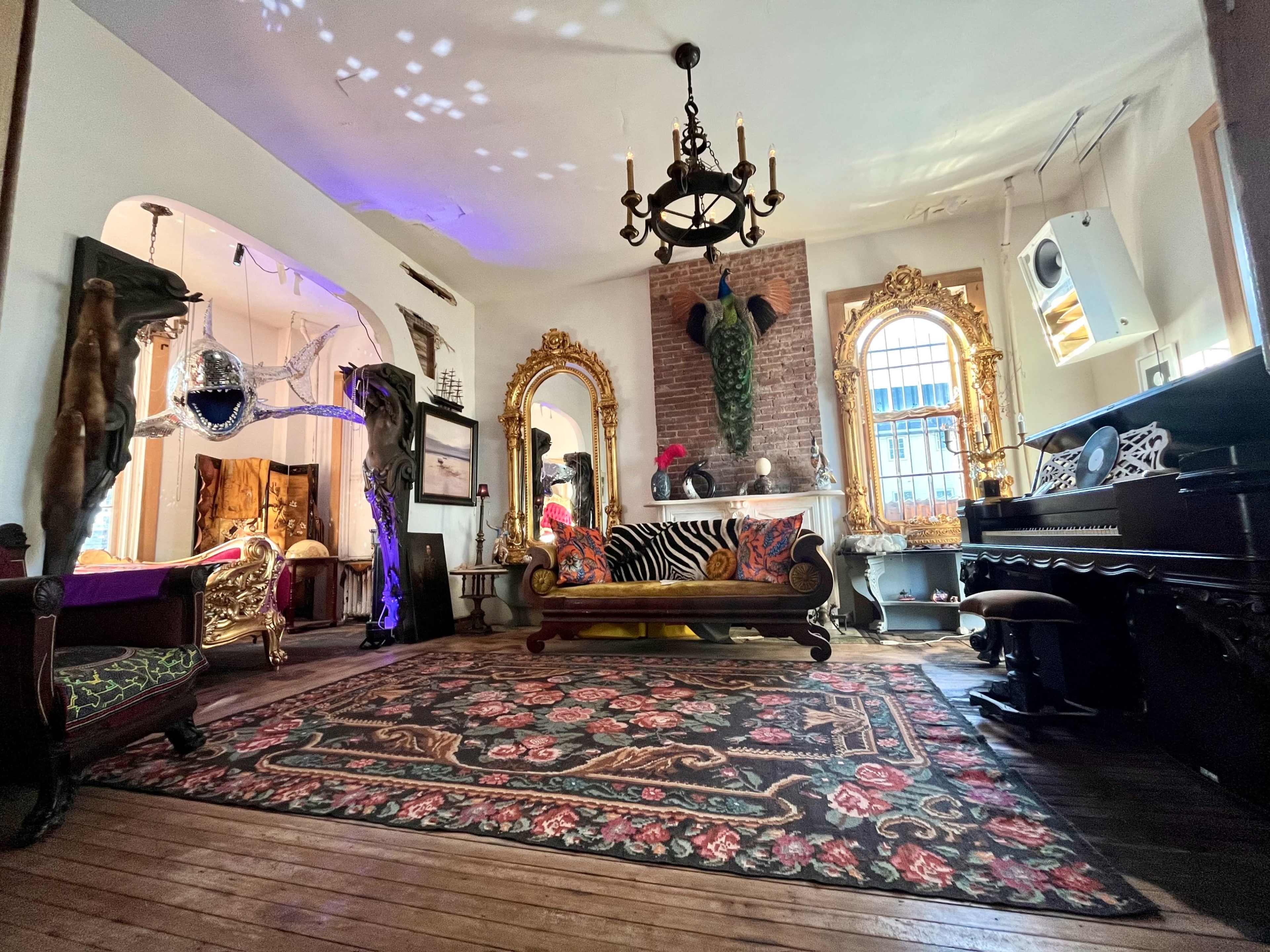 A creatively decorated living room featuring eclectic furnishings, including a zebra-striped sofa, ornate mirrors, and artistic sculptures.