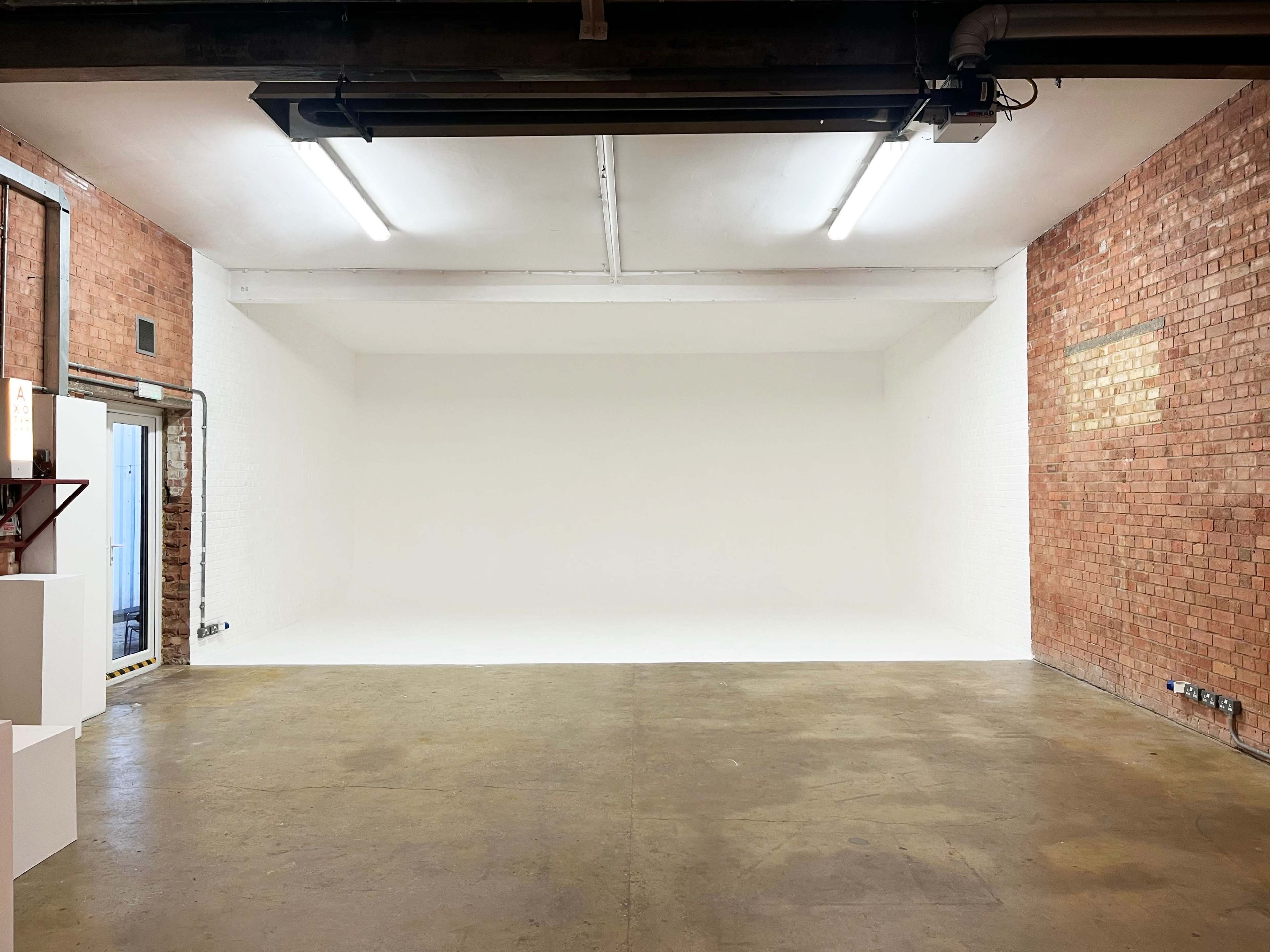 A spacious interior room with brick walls, a white backdrop, and concrete flooring.