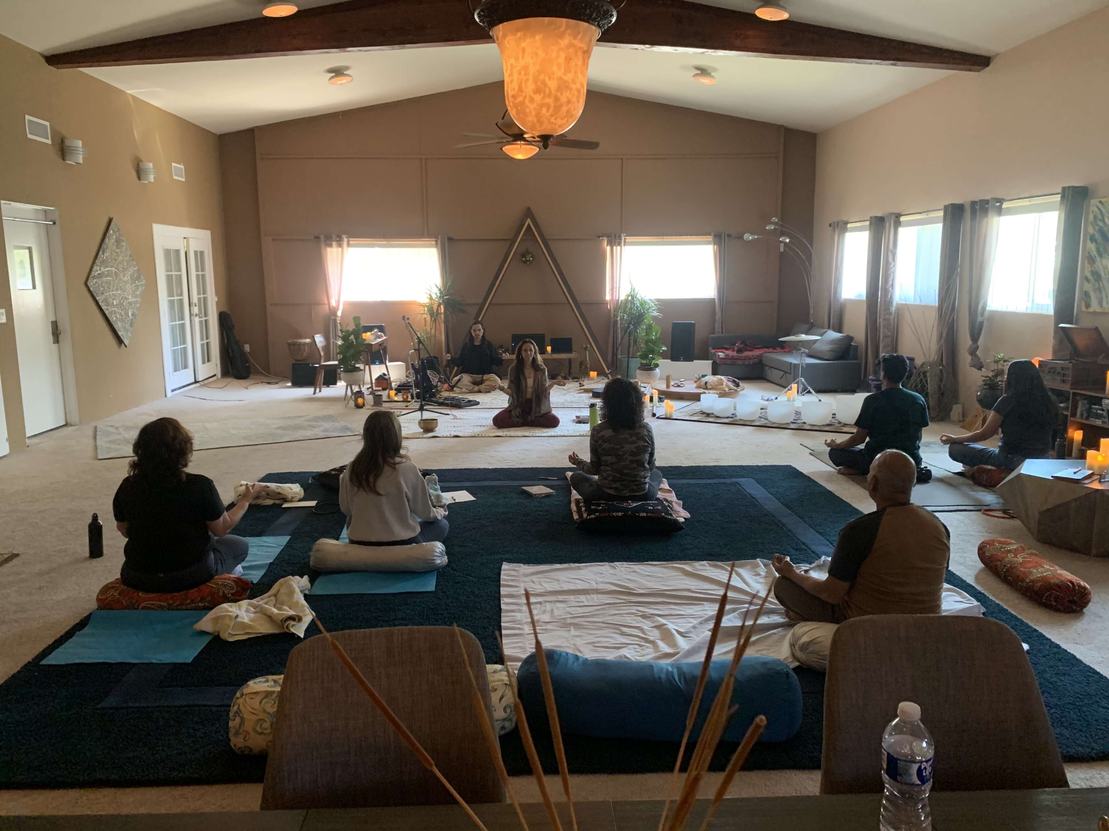 A group of individuals sits on mats in a serene, spacious room arranged for a meditation or wellness session.