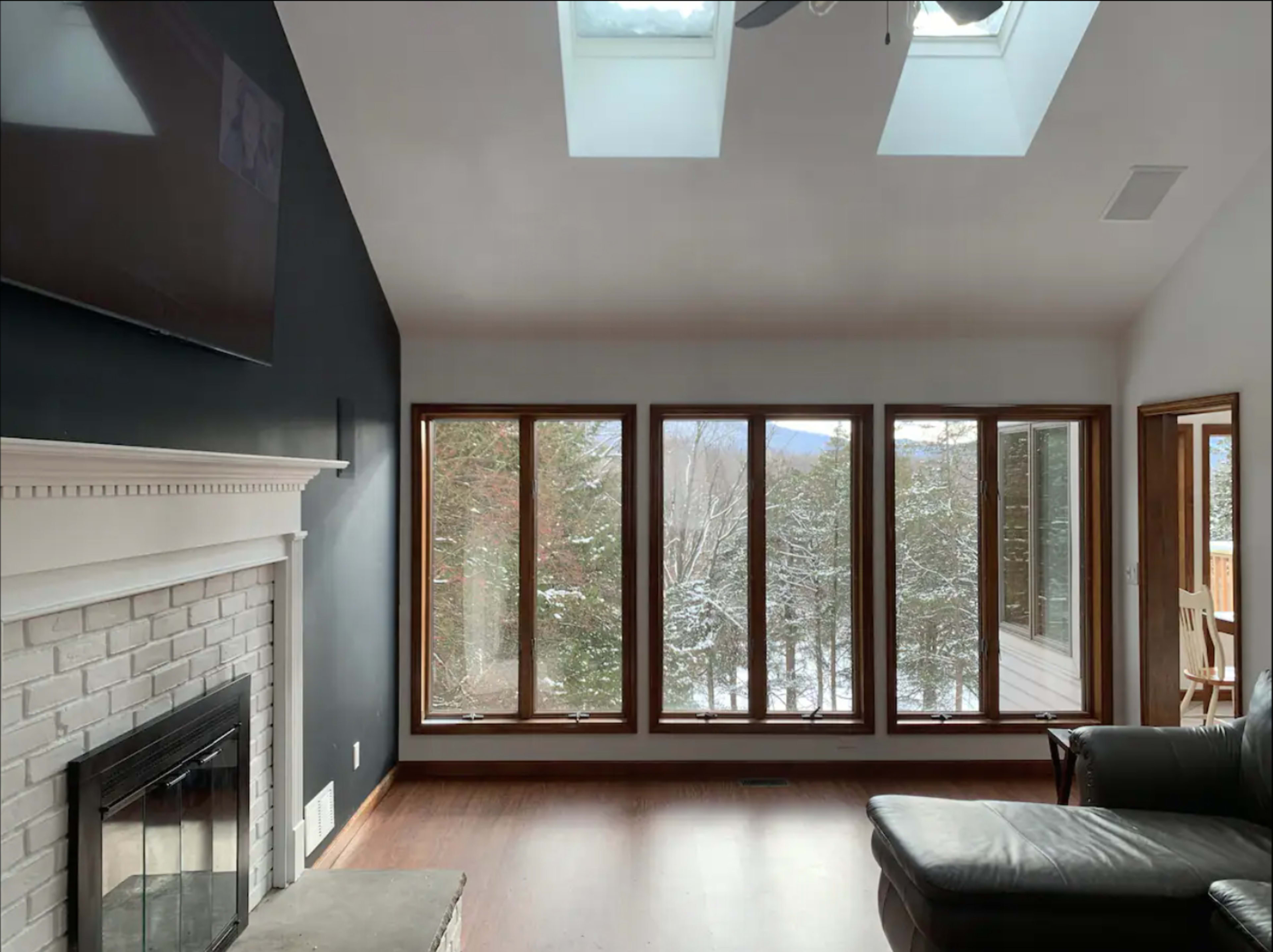 A living room features a brick fireplace and large windows overlooking a snowy outdoor landscape.