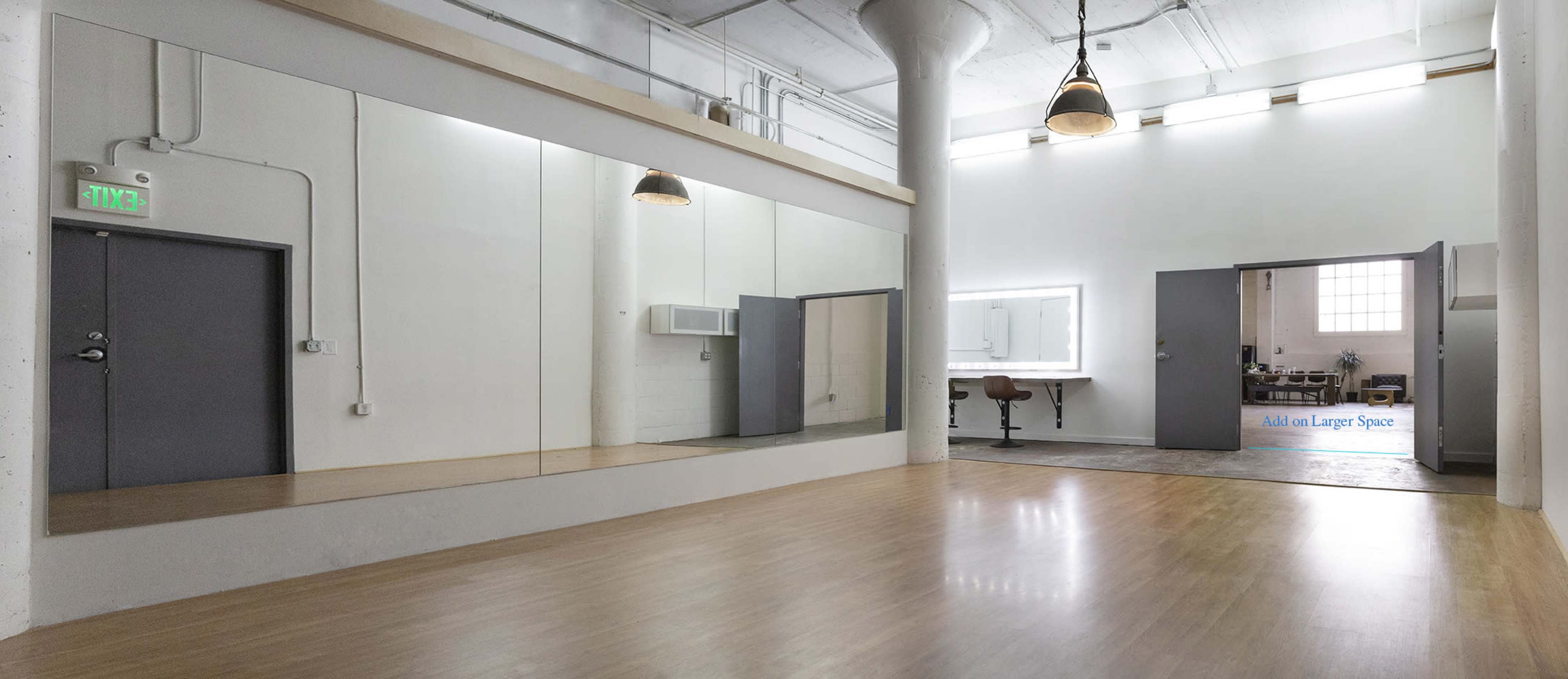 The image shows a spacious, well-lit studio with a large mirror on one wall and a bathroom visible through an open door in the background.