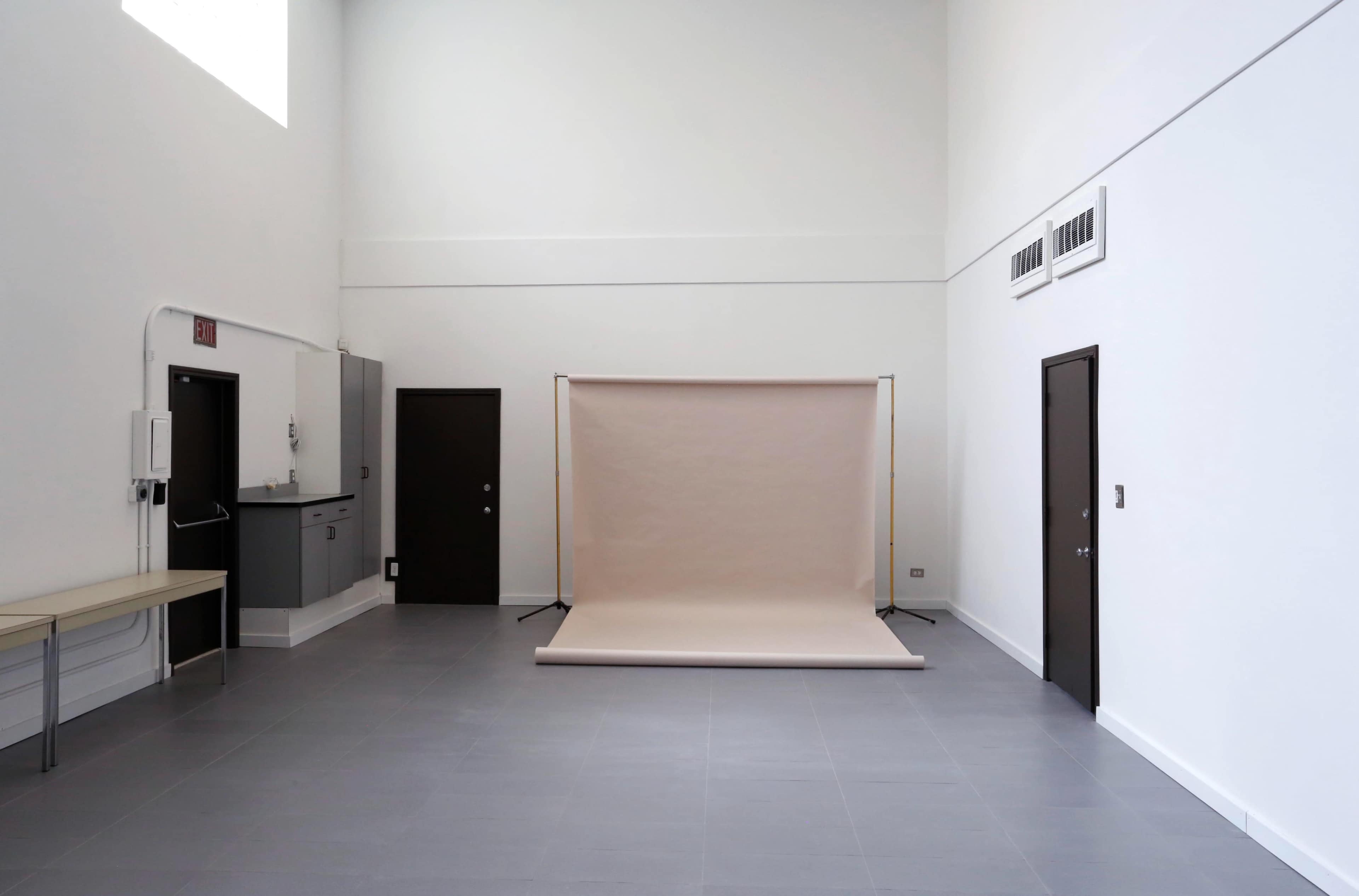 A spacious, minimalistic room with grey tiled flooring, a beige backdrop on a stand, and doors along the walls.