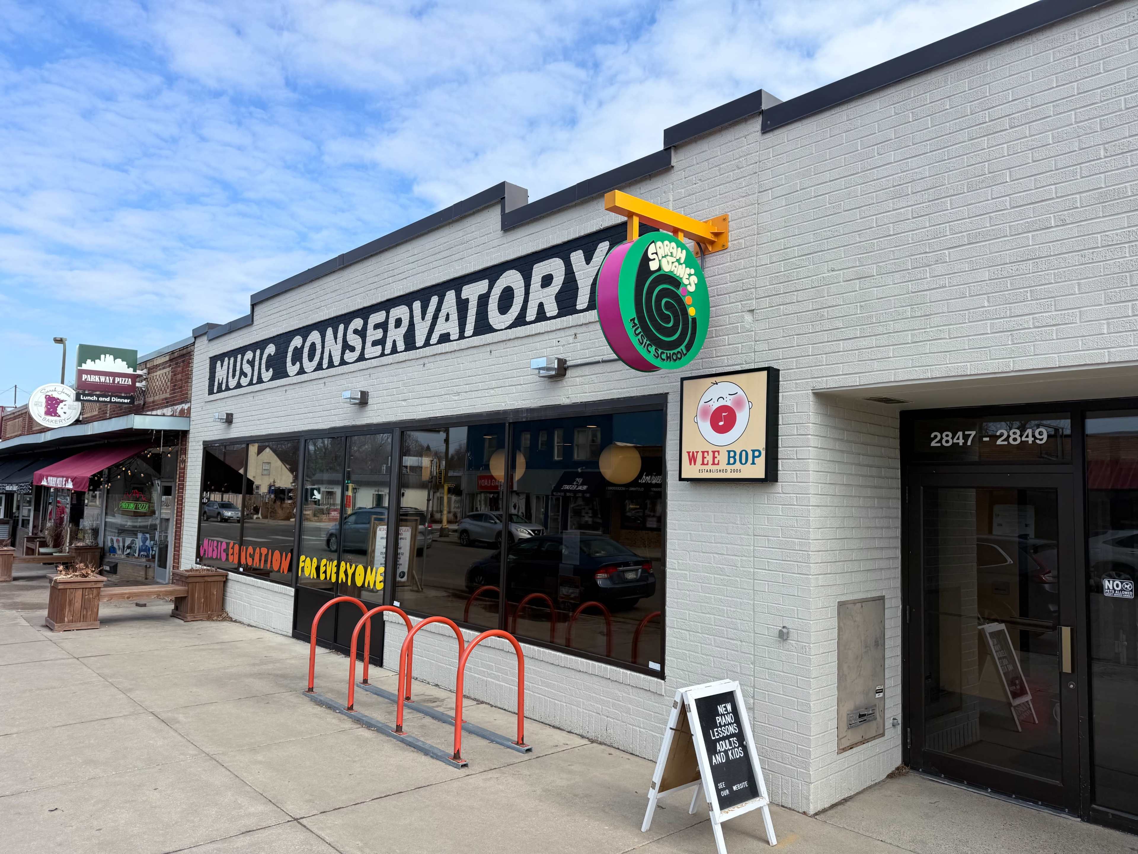 The image shows a storefront labeled "Music Conservatory" with a colorful sign above it, and a smaller sign for "Wee Bop" on the side.