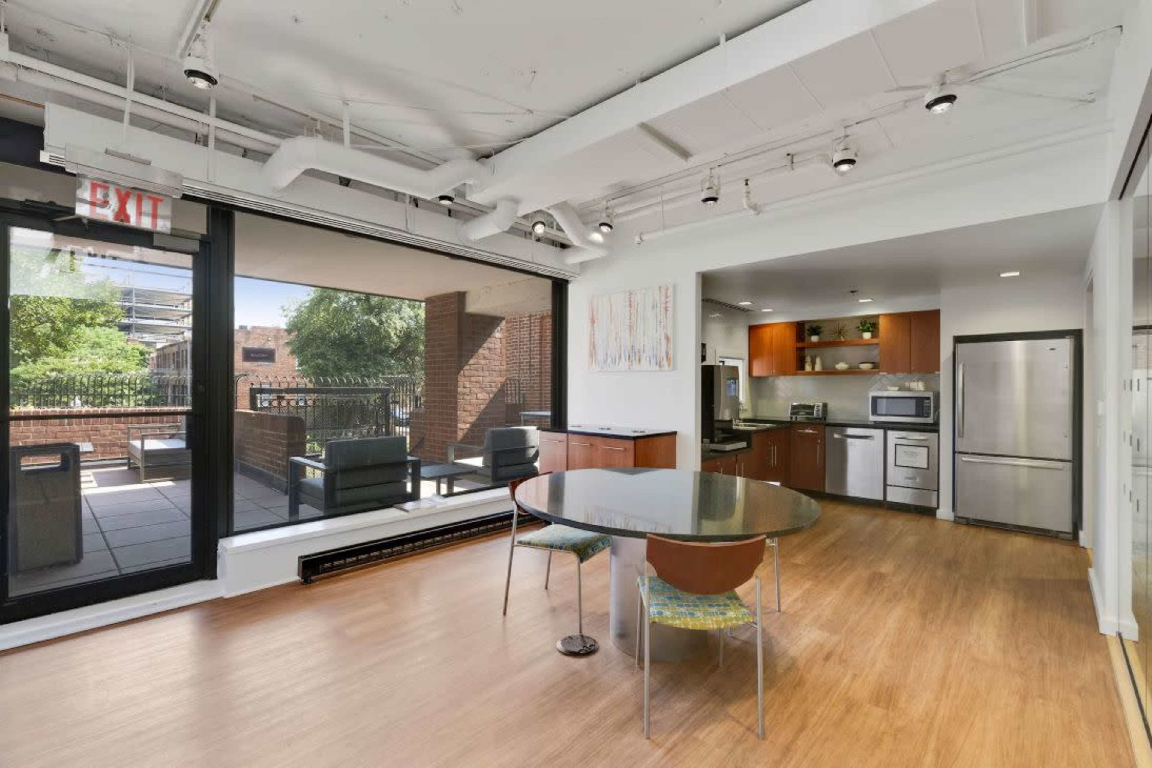 The image shows a modern kitchen and dining area featuring a circular table, sleek cabinetry, and large windows that open to an outdoor terrace.