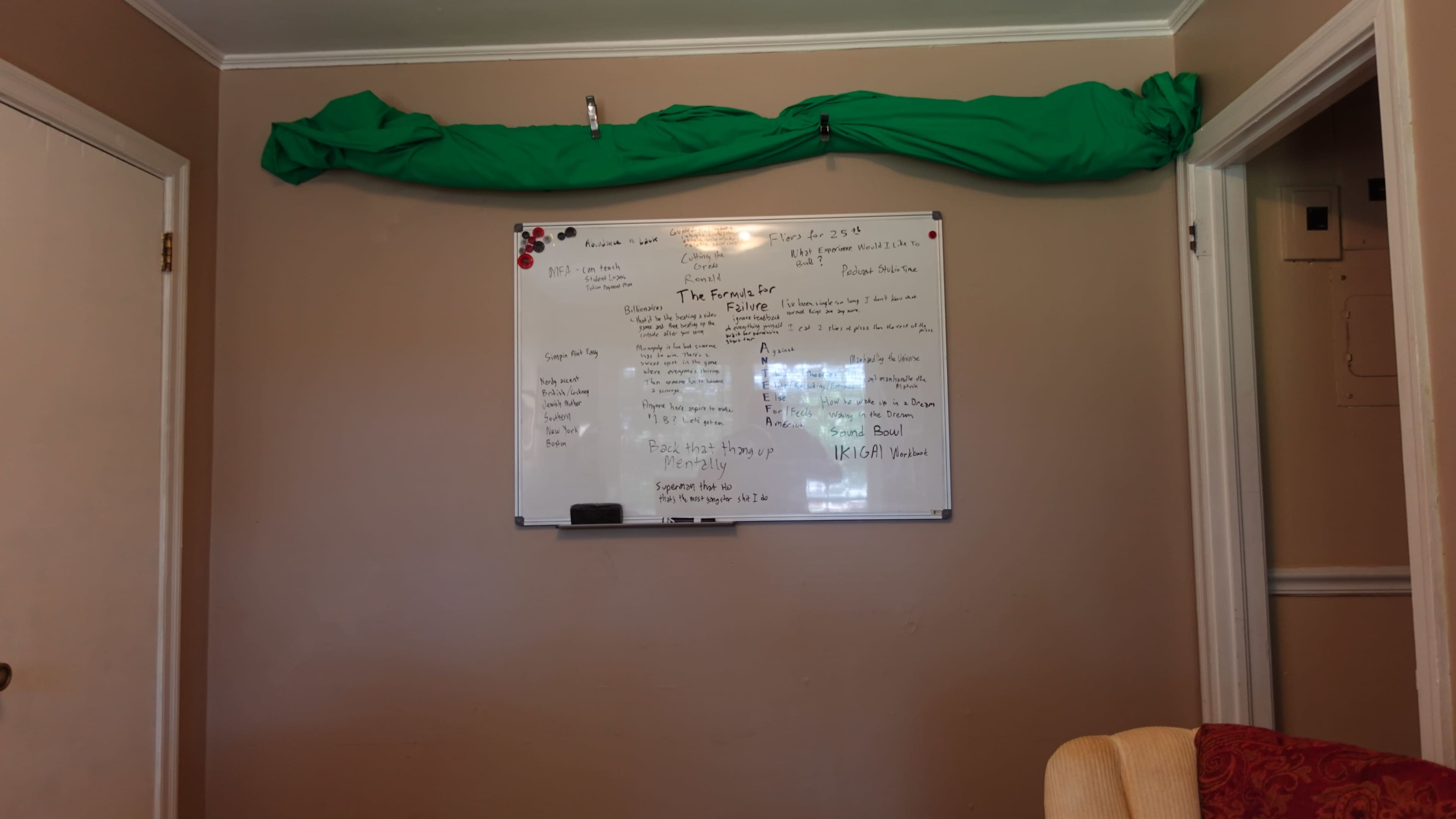 A green fabric drapes over a wall above a whiteboard filled with handwritten notes and lists.