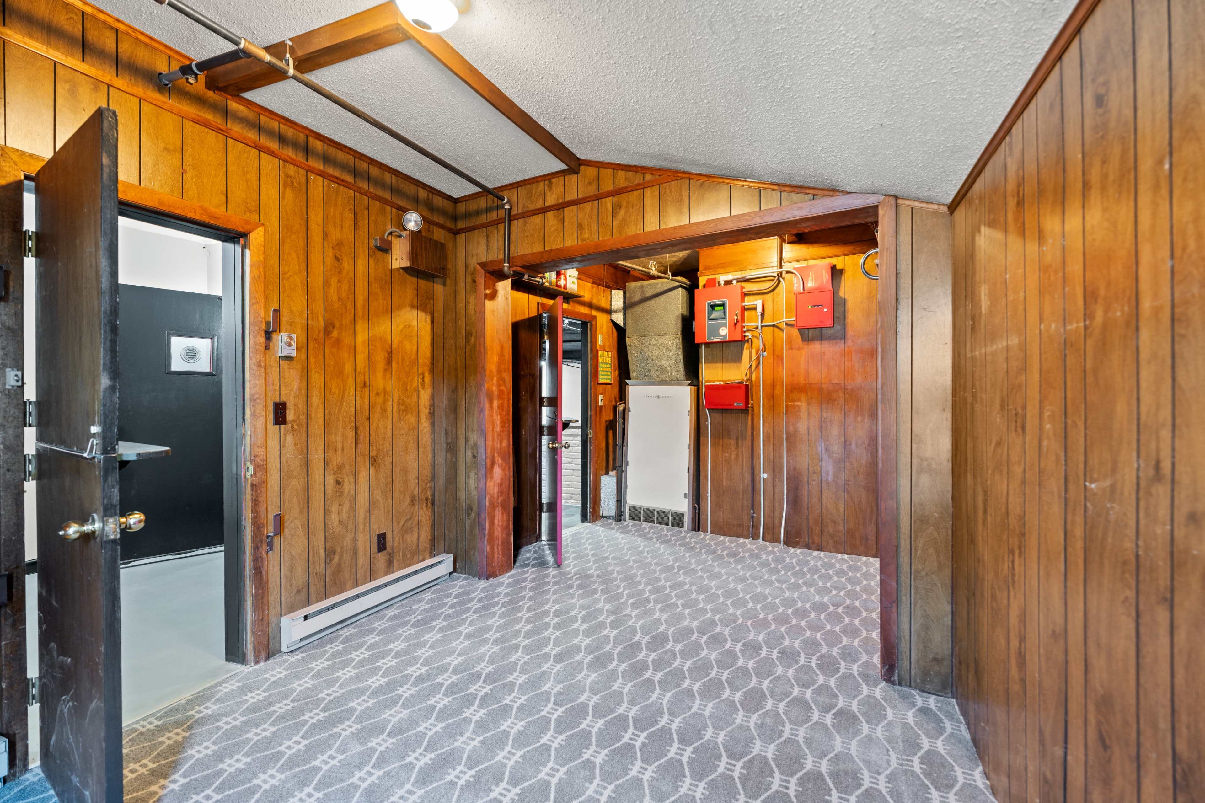 The image shows a room with wooden paneling, a patterned carpet, and several electrical panels mounted on the wall.