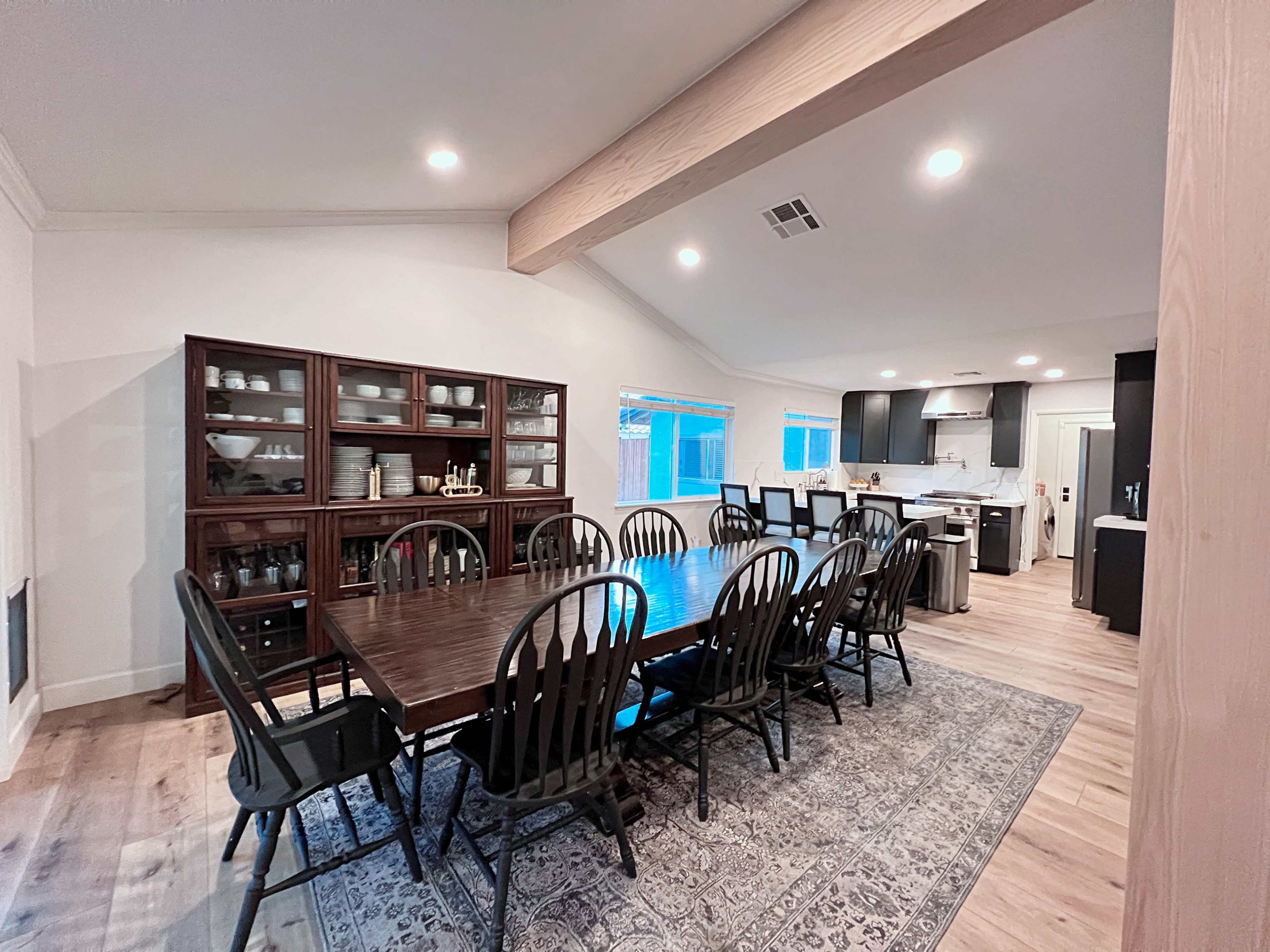 A spacious dining area with a large table surrounded by chairs, adjacent to a modern kitchen.