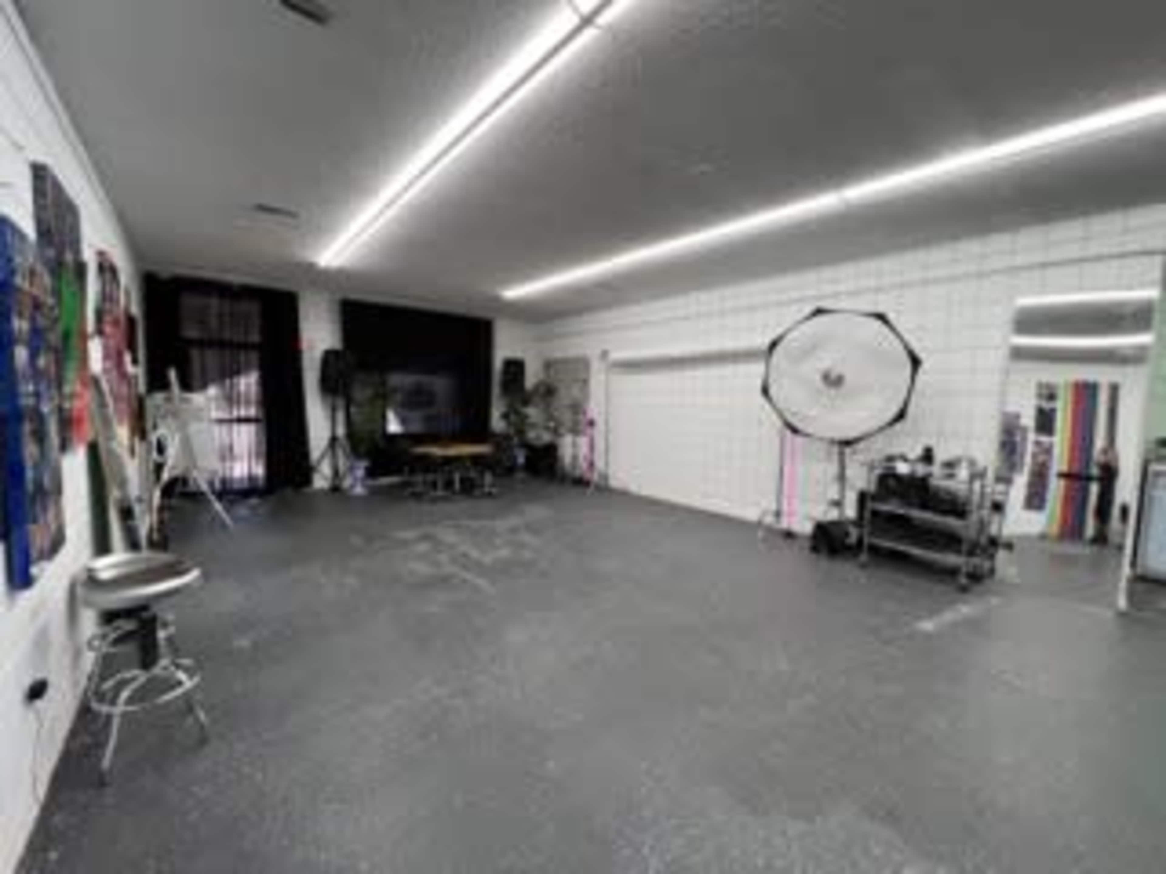 A spacious studio with a gray floor, white walls, and a large softbox lighting setup in one corner.