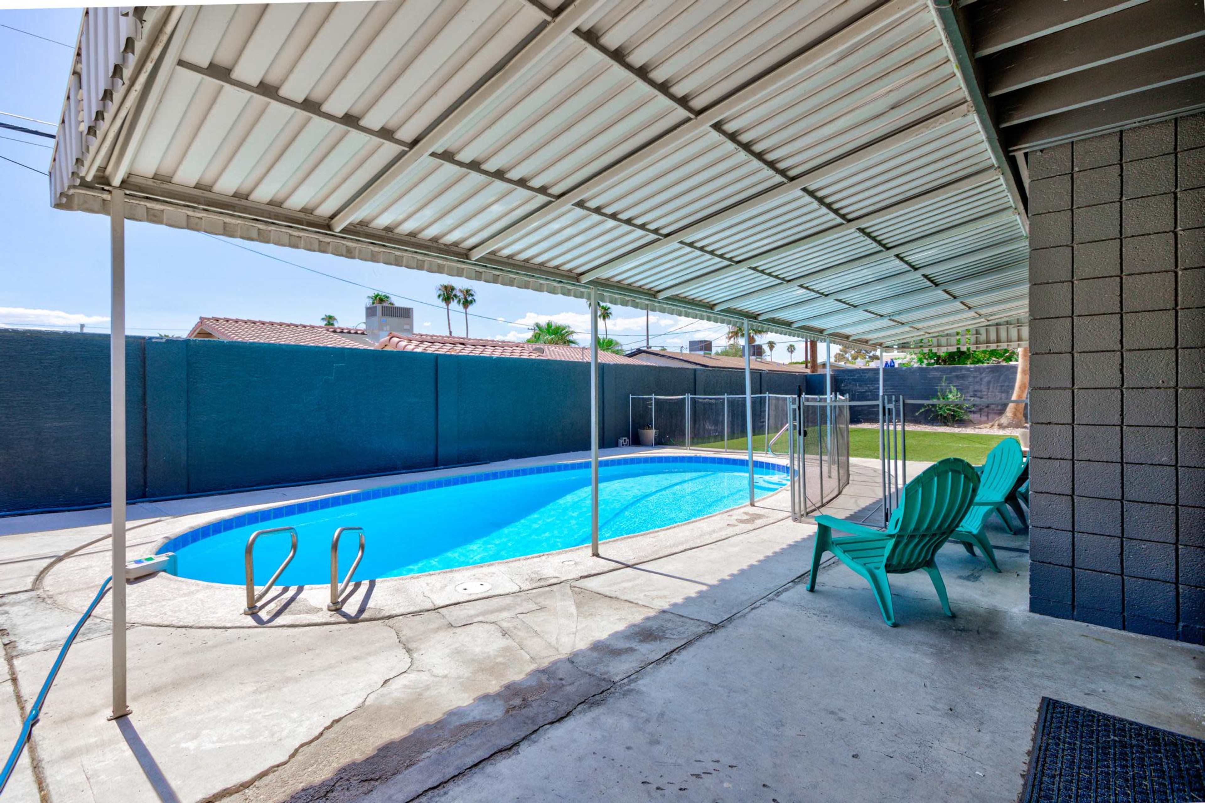 The image shows a swimming pool area with a covered patio and green lounge chairs positioned beside the pool.