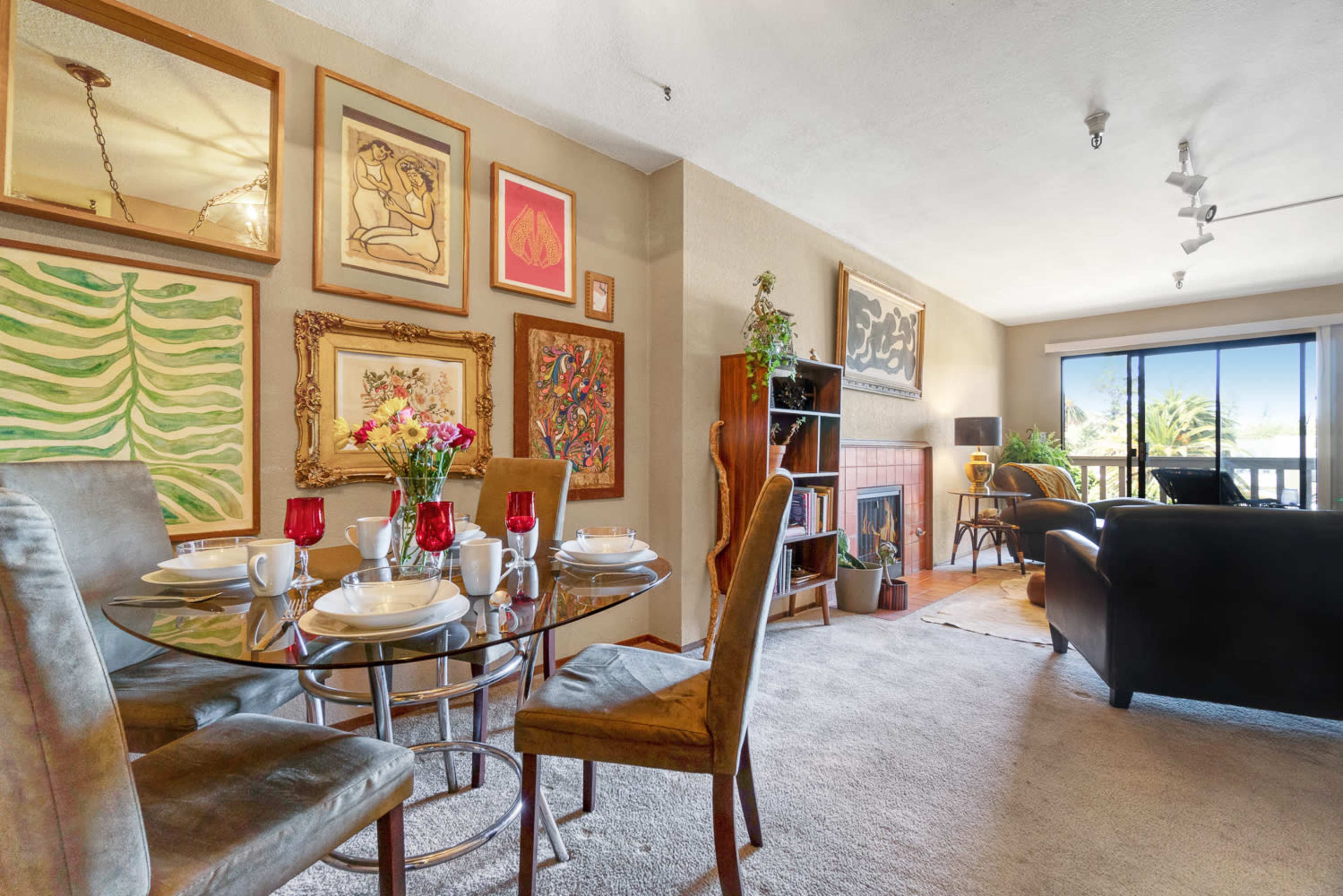 A cozy living area with a dining table set for four, surrounded by decorative wall art and a view of a balcony.