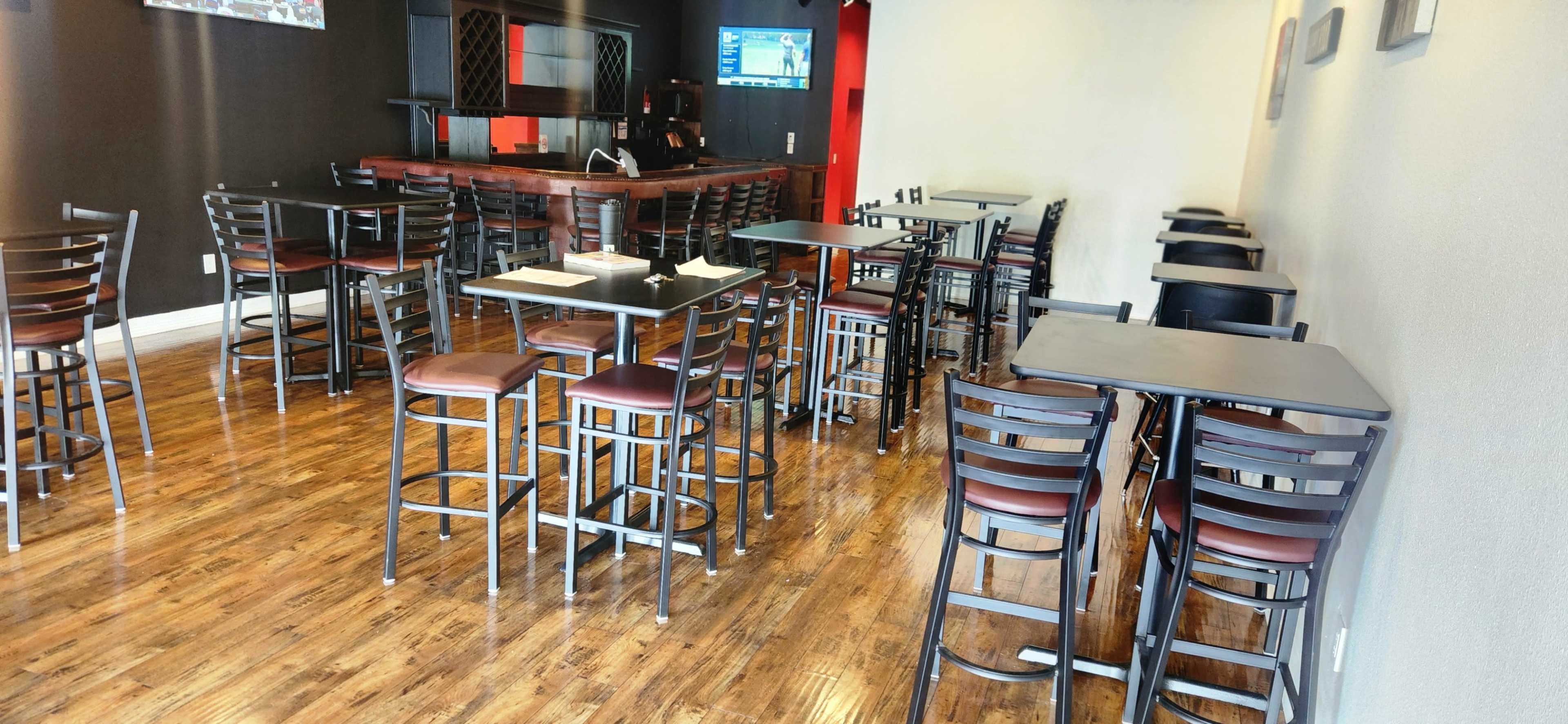 The image shows an empty dining area with metal tables and chairs, a wooden floor, and a bar in the background.