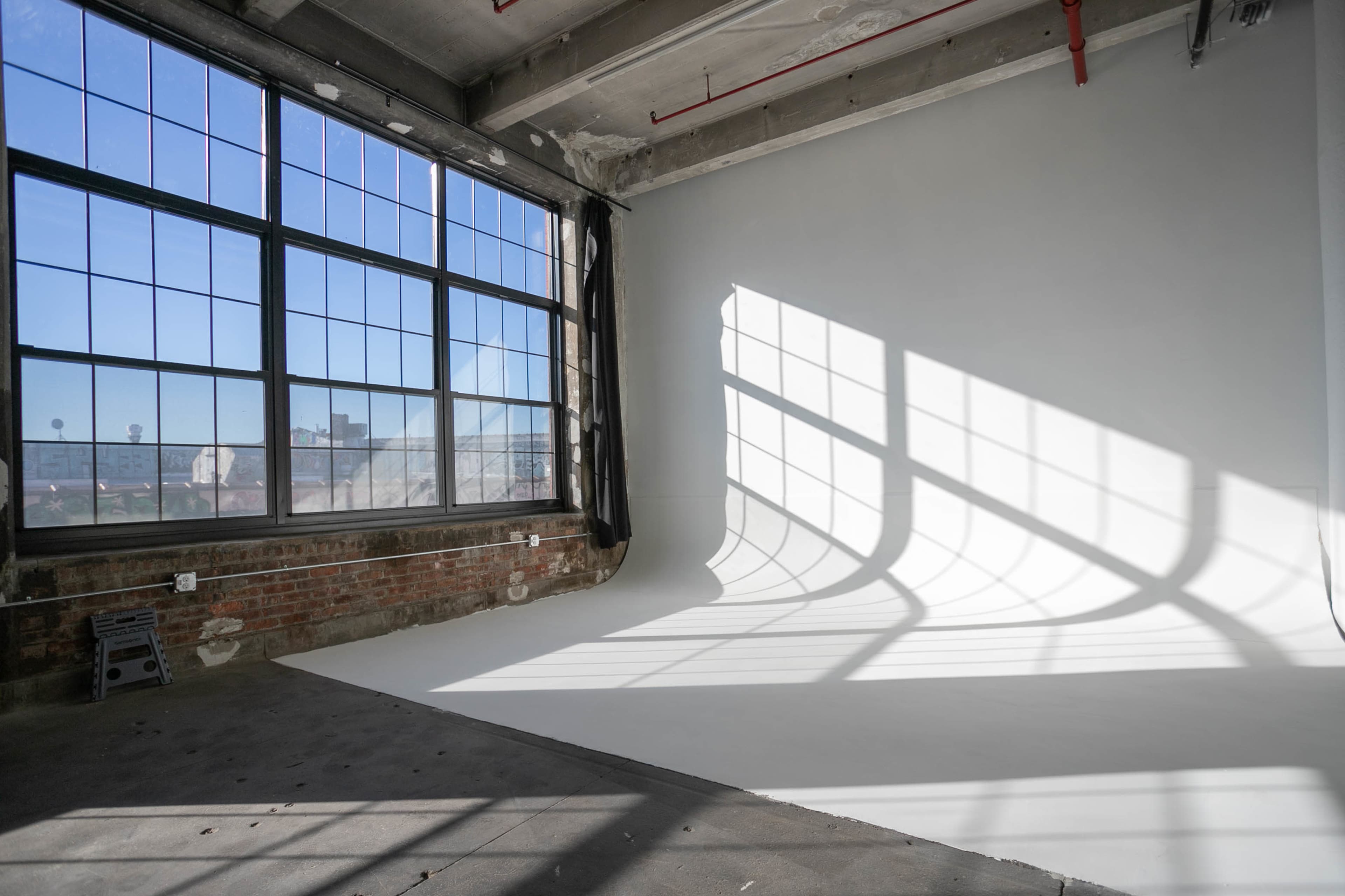 A spacious room with large windows casts shadows on a white wall and floor.