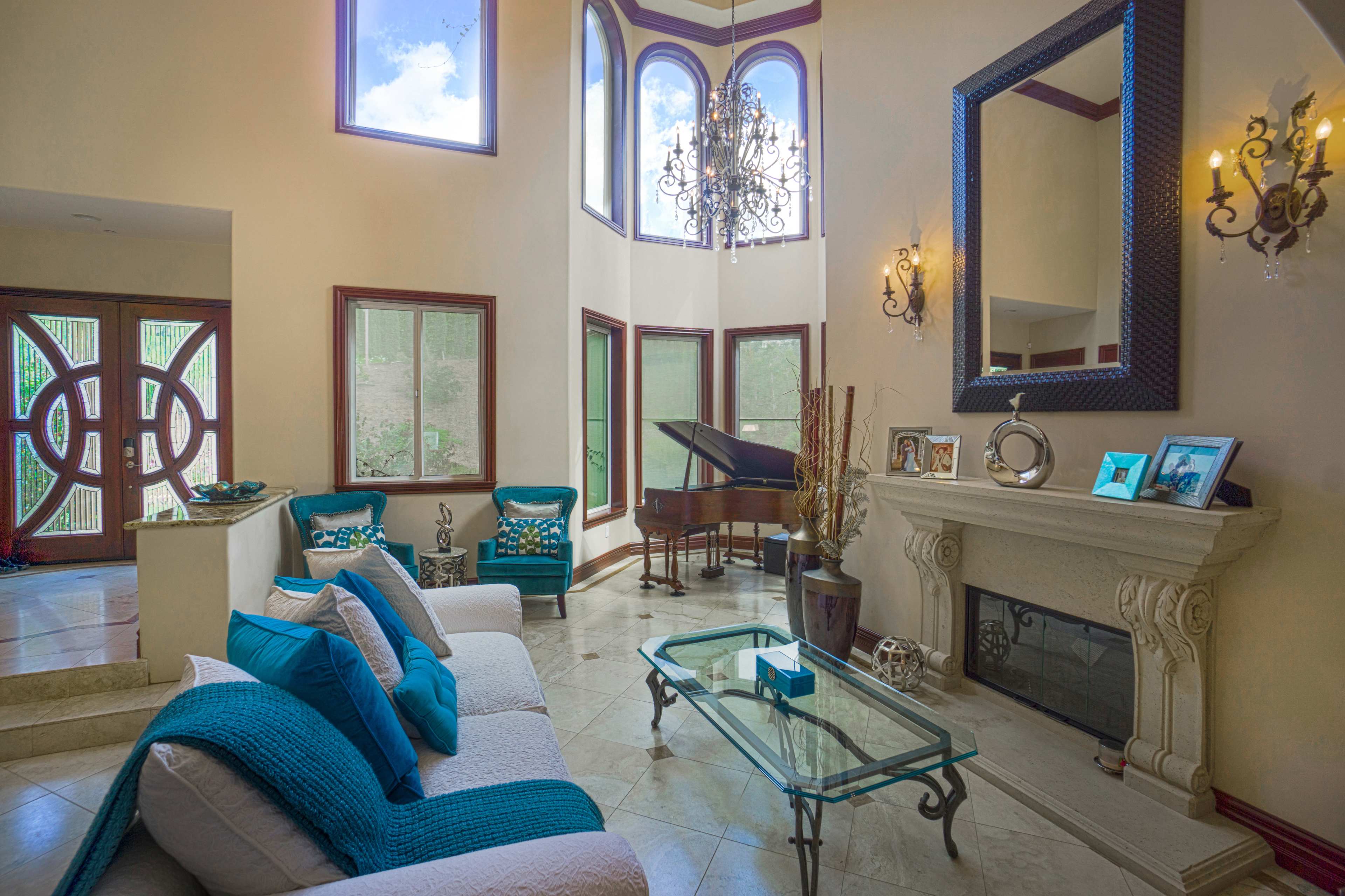 The image shows a brightly lit living room featuring a grand piano, a marble floor, and large windows adorned with decorative frames.