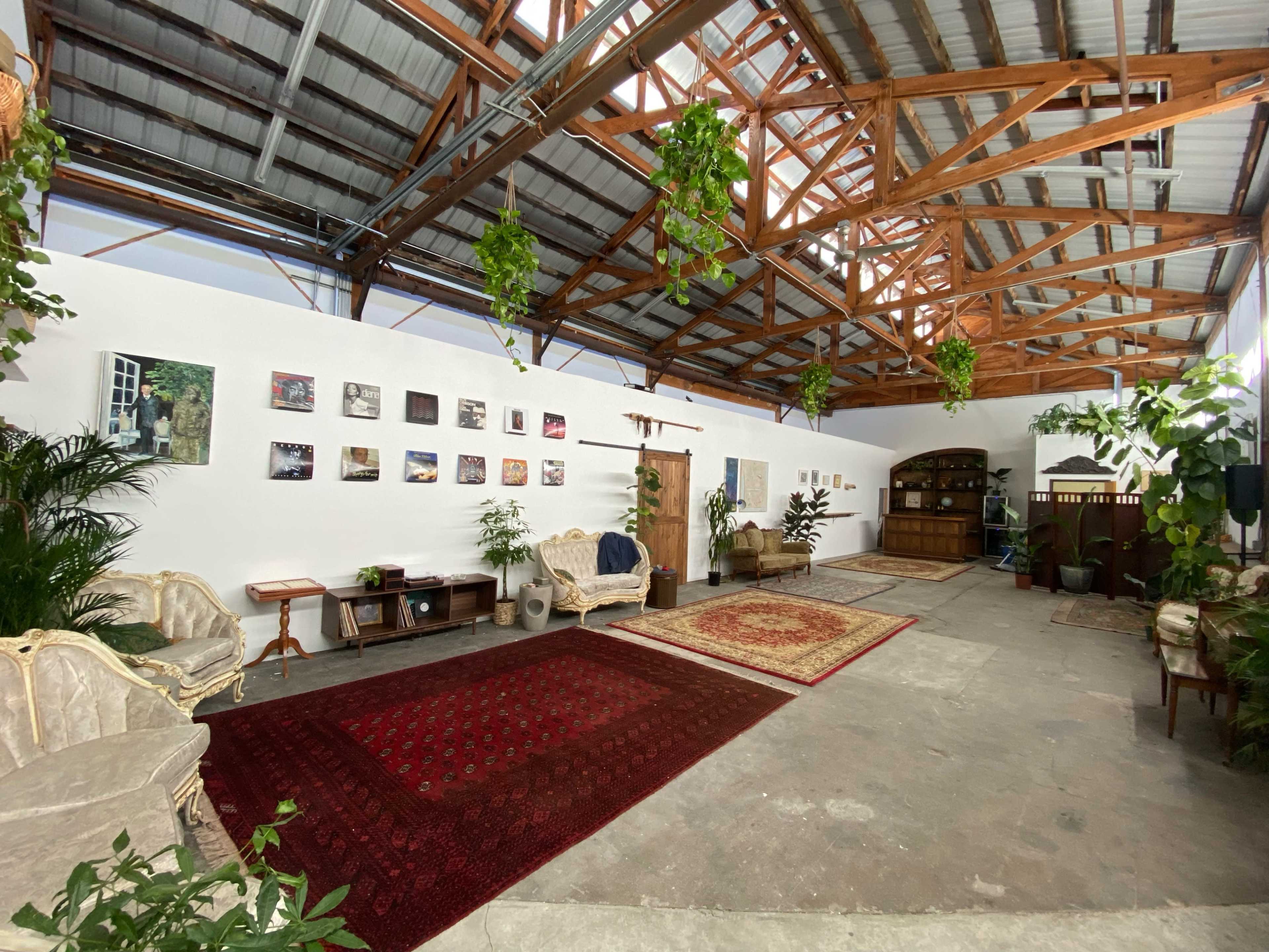 An open, airy space with a high wooden ceiling, featuring seating areas, wall-mounted artwork, and various plants.