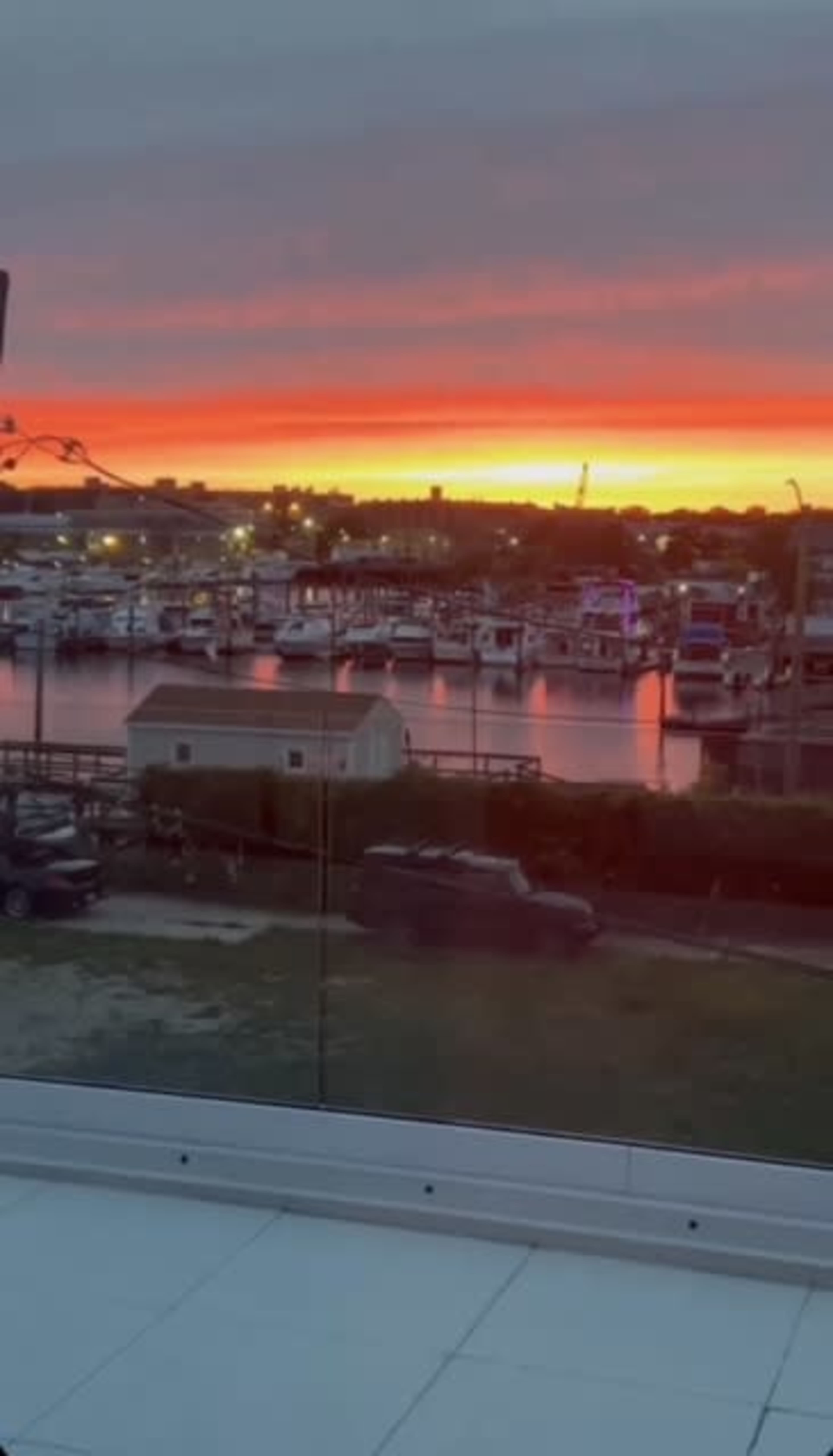 The image shows a marina at sunset, with boats docked and colorful skies reflecting on the water.