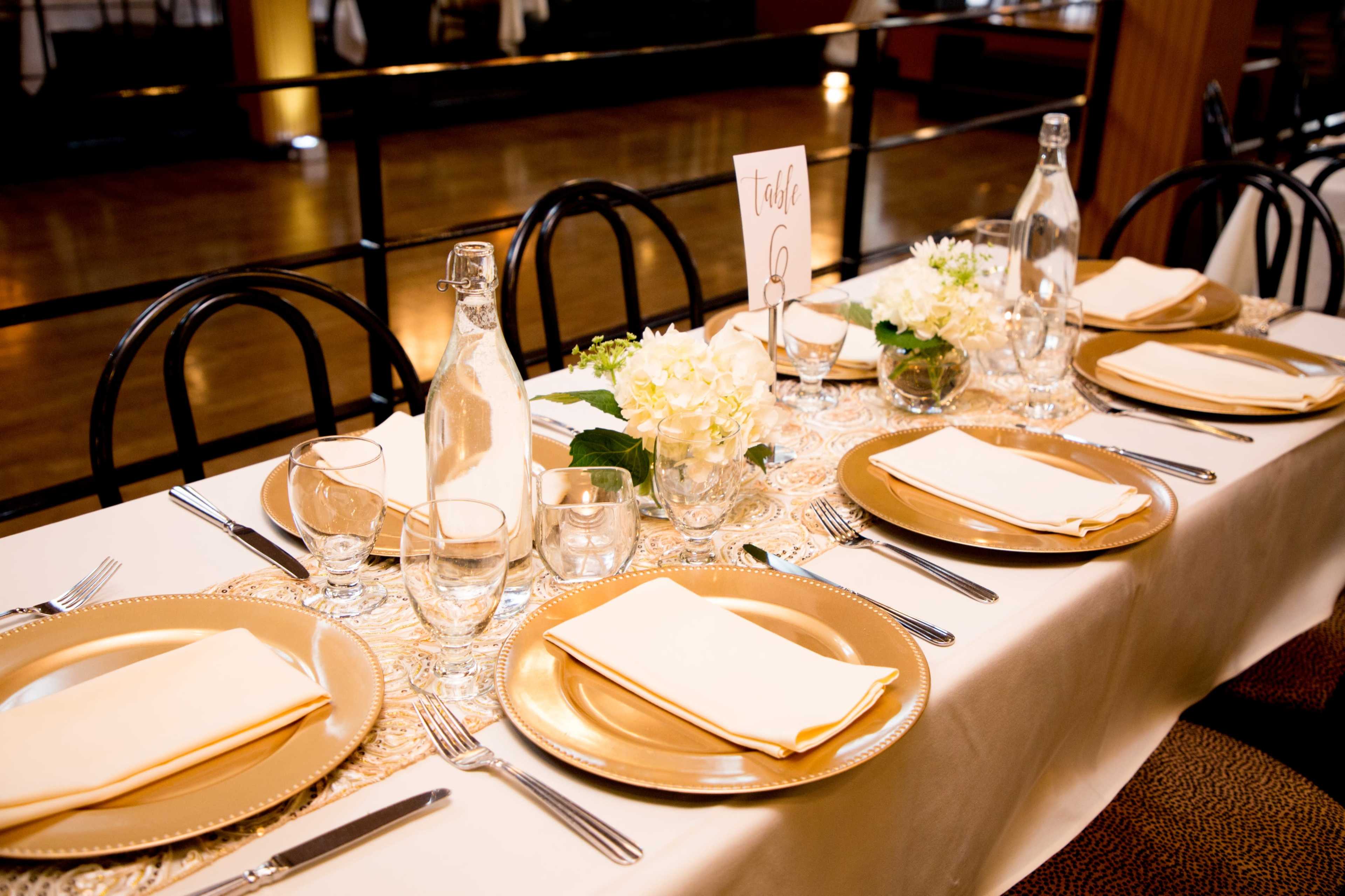 A beautifully set dining table features gold-rimmed plates, glassware, and floral centerpieces, ready for an elegant meal.