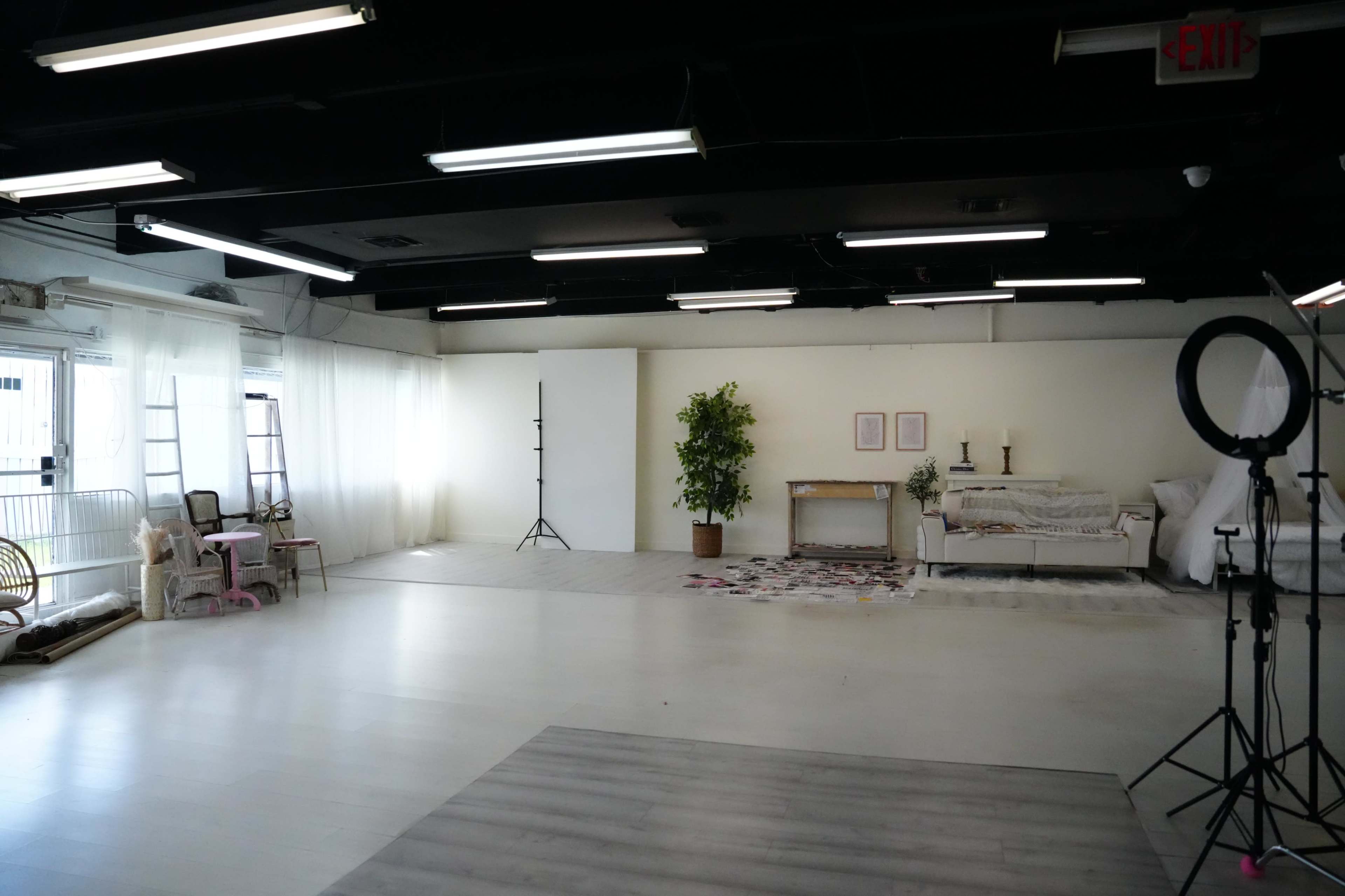 A spacious studio with various furniture arrangements, including a sofa, a table, and backdrop equipment, set against white walls and ceiling lights.