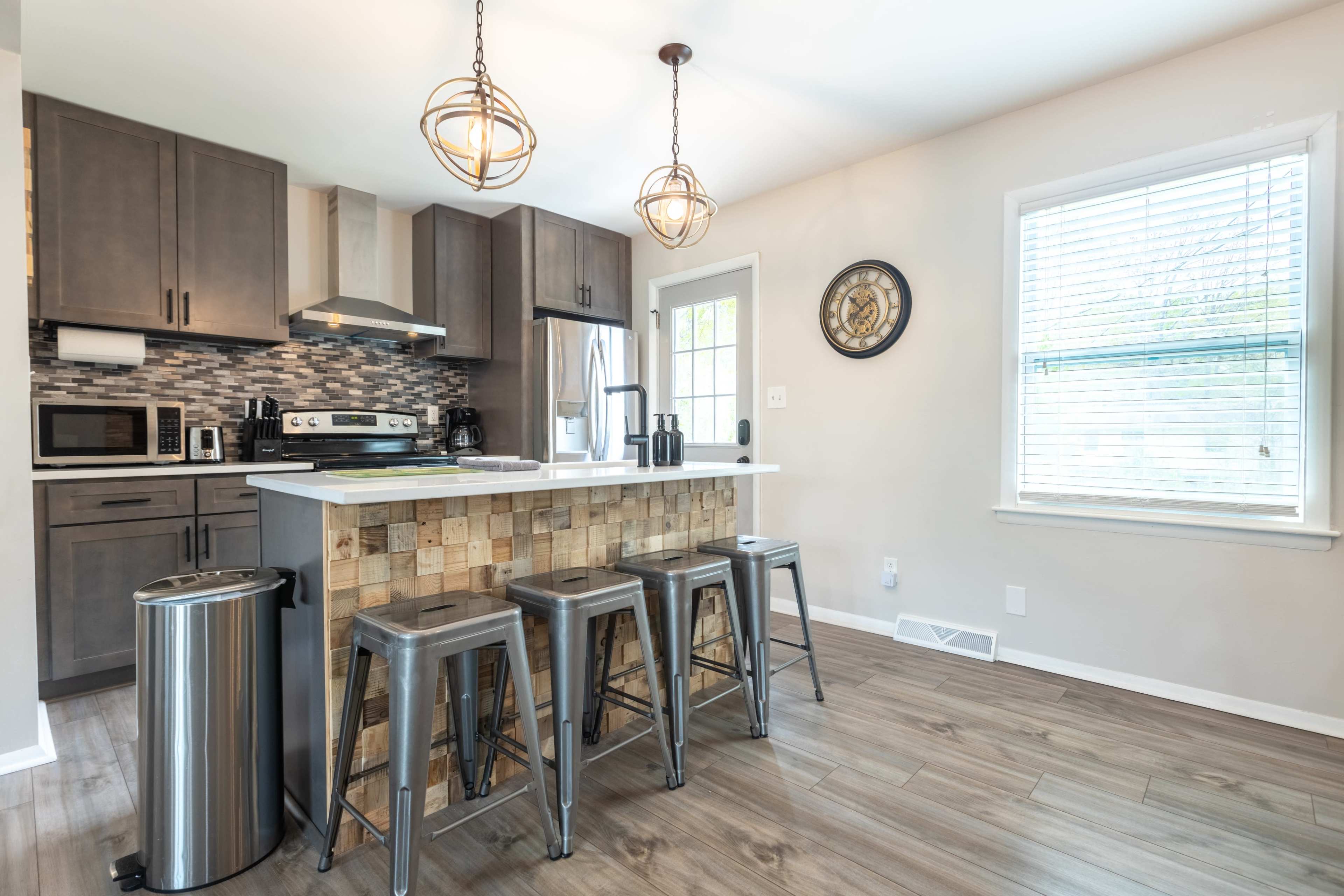 A modern kitchen features gray cabinetry, stainless steel appliances, and a wooden-paneled island with metal bar stools.
