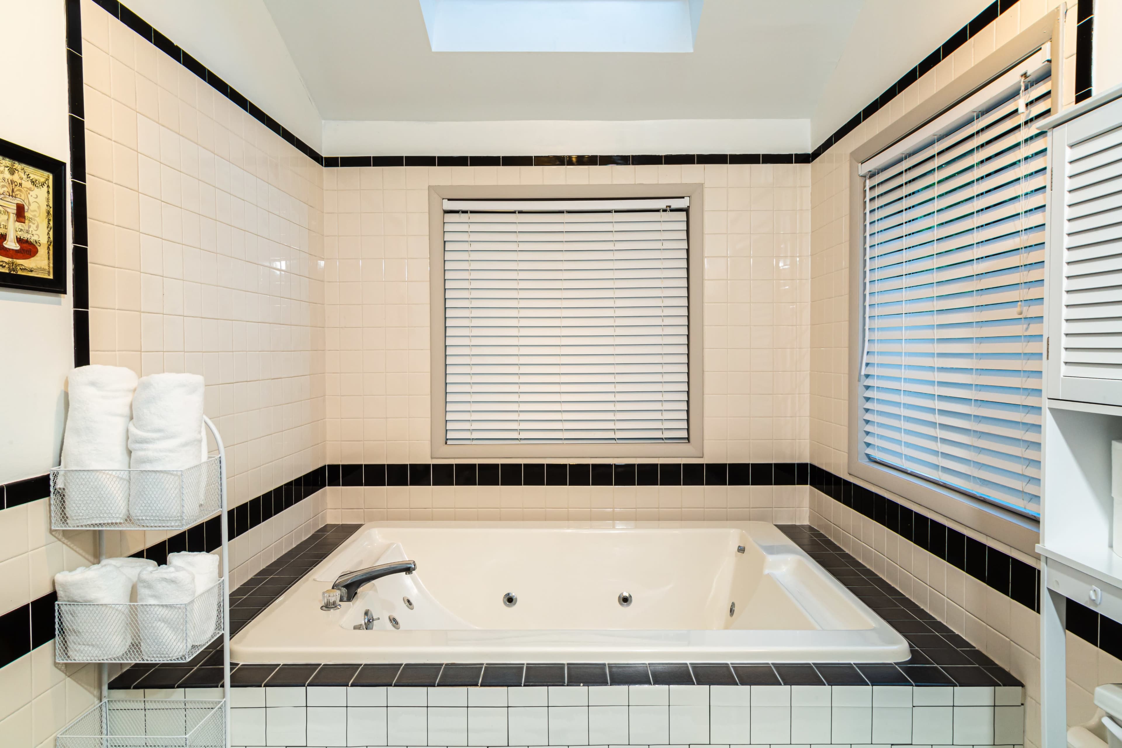 A modern bathroom with a whirlpool tub surrounded by tiled walls and a window covered by blinds.