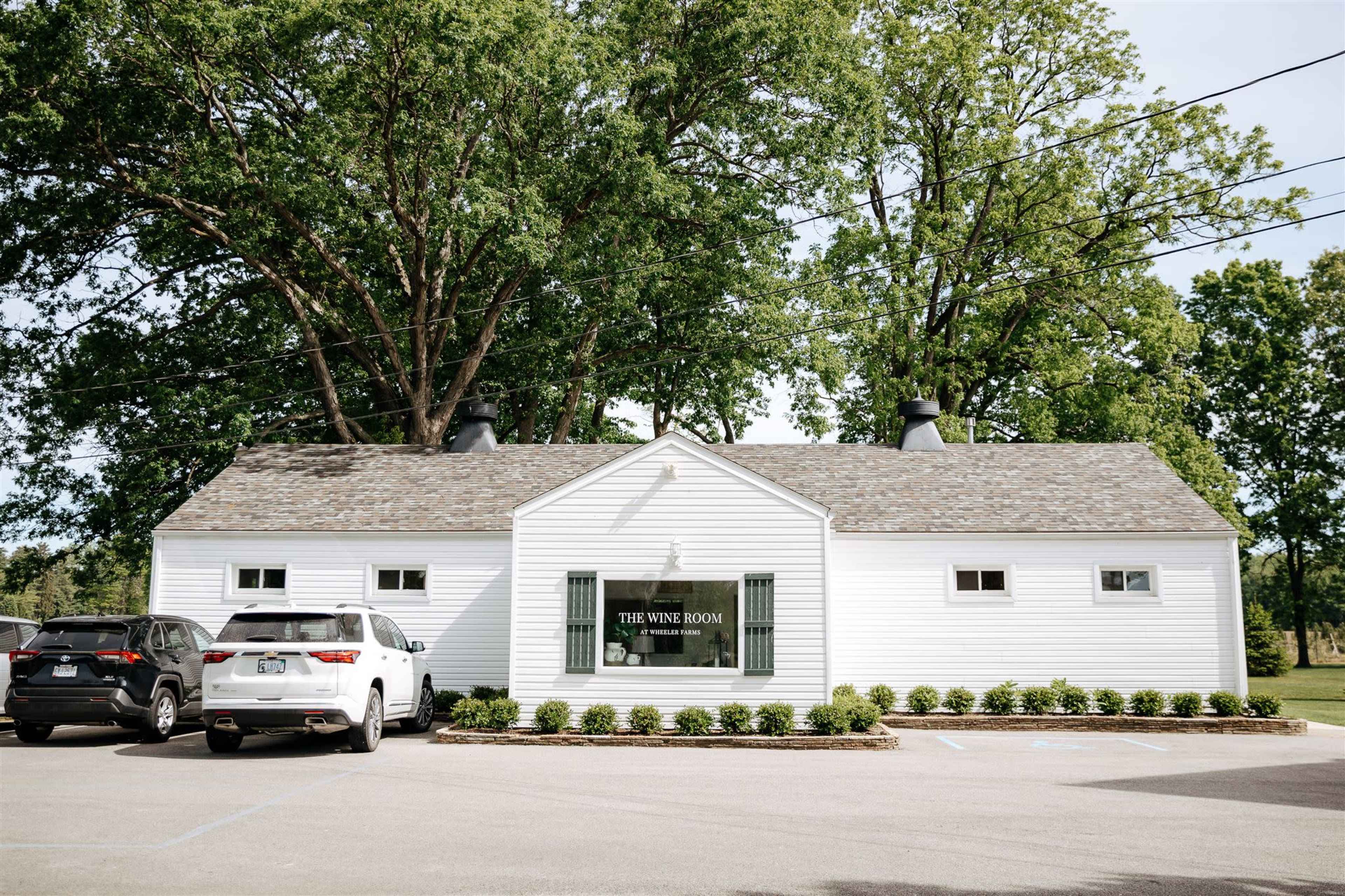 The image shows a white building with a sign reading "THE WINE ROOM," surrounded by trees and parked cars.