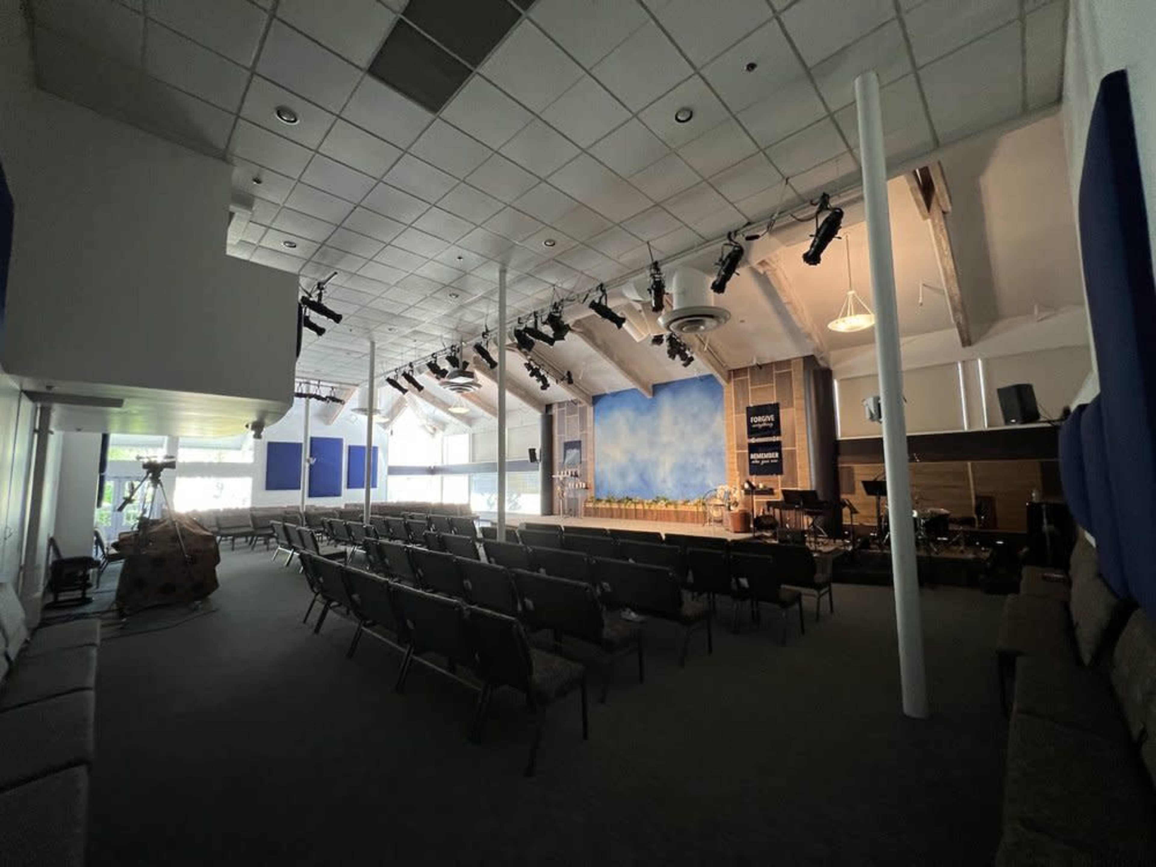 A spacious indoor auditorium with rows of chairs facing a stage, which features a blue backdrop and musical instruments set up.