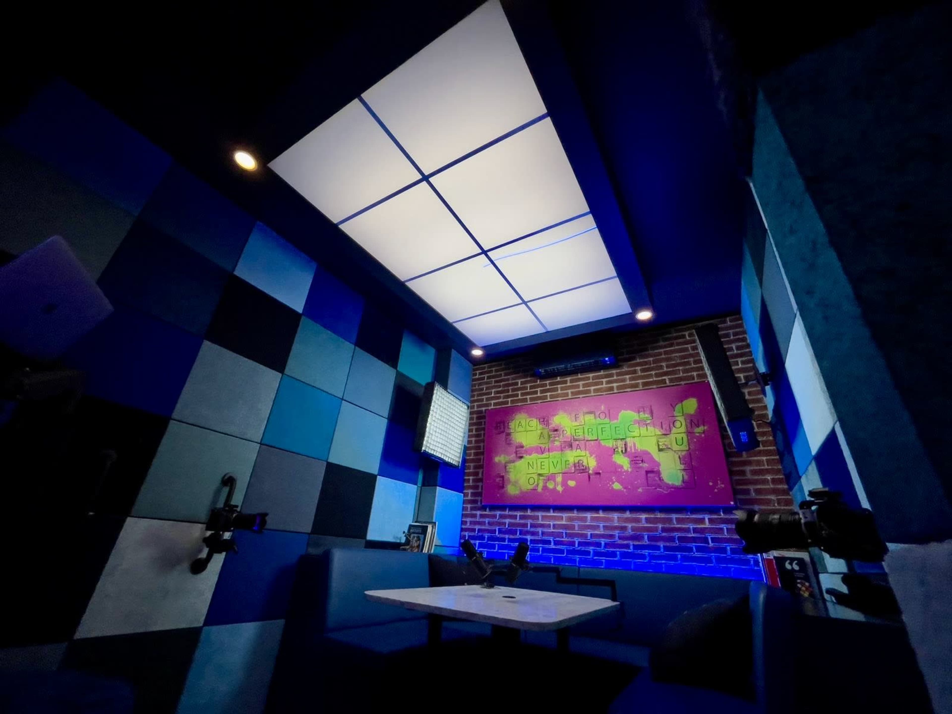 The image shows a small, modern room with blue and gray walls, a map on the back wall, and a central table surrounded by seating.