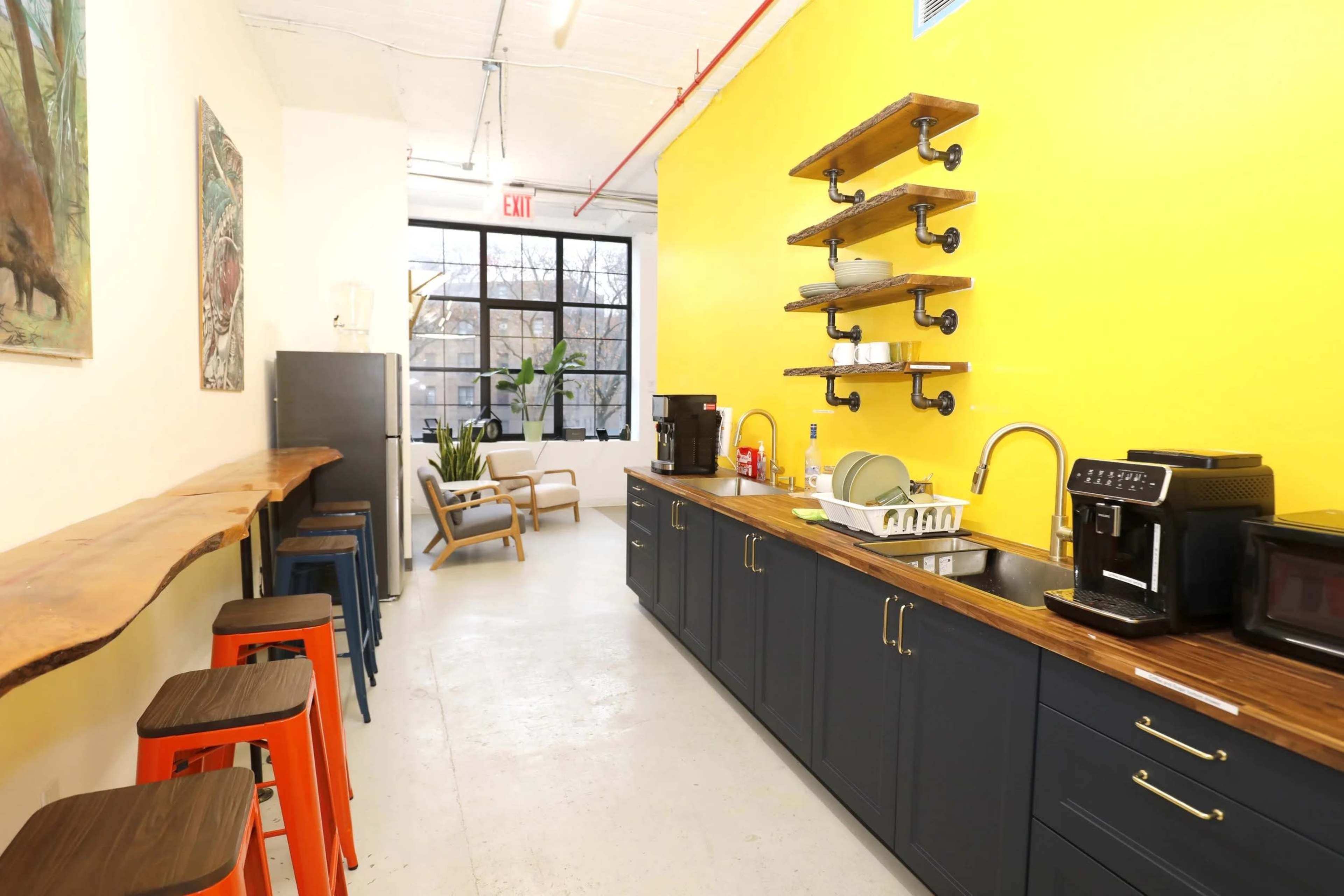 The image shows a modern kitchen area with a yellow wall, a wood countertop, and various appliances including a coffee maker and sink.