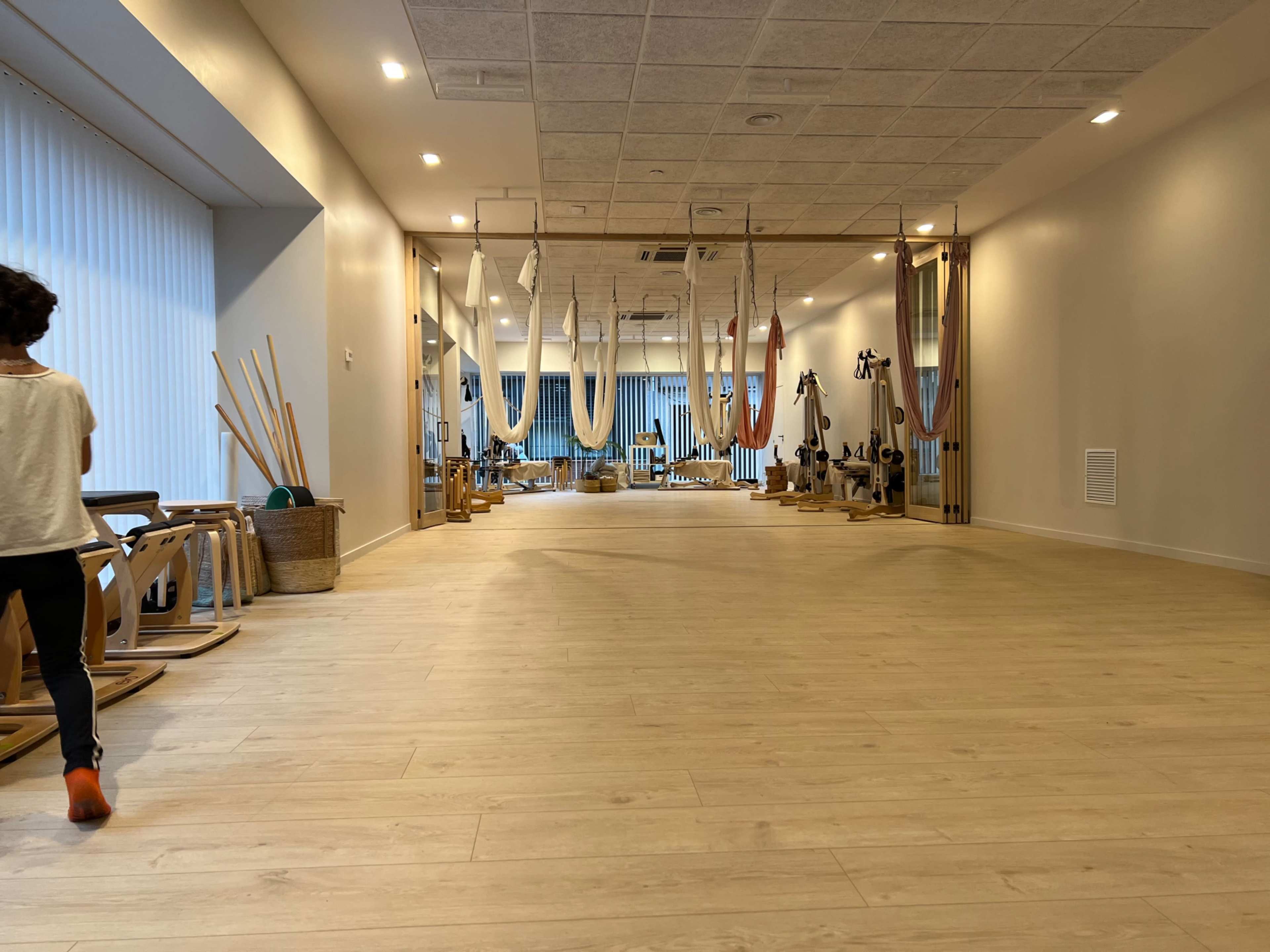 A spacious studio features wooden floors, exercise equipment, and several suspended hammocks hanging from the ceiling.