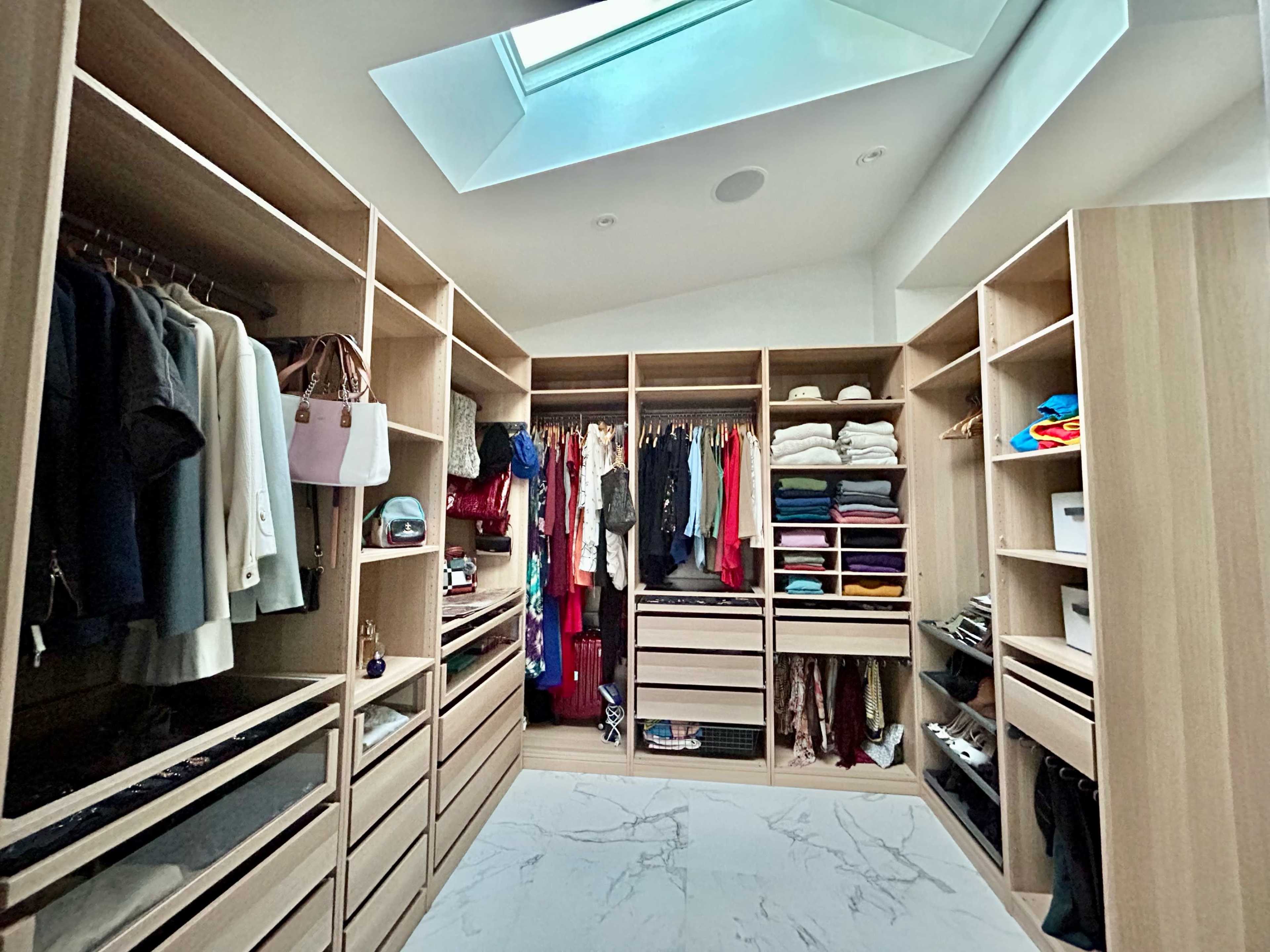 A spacious walk-in closet features organized shelves and hanging areas filled with clothing and accessories, illuminated by a skylight above.