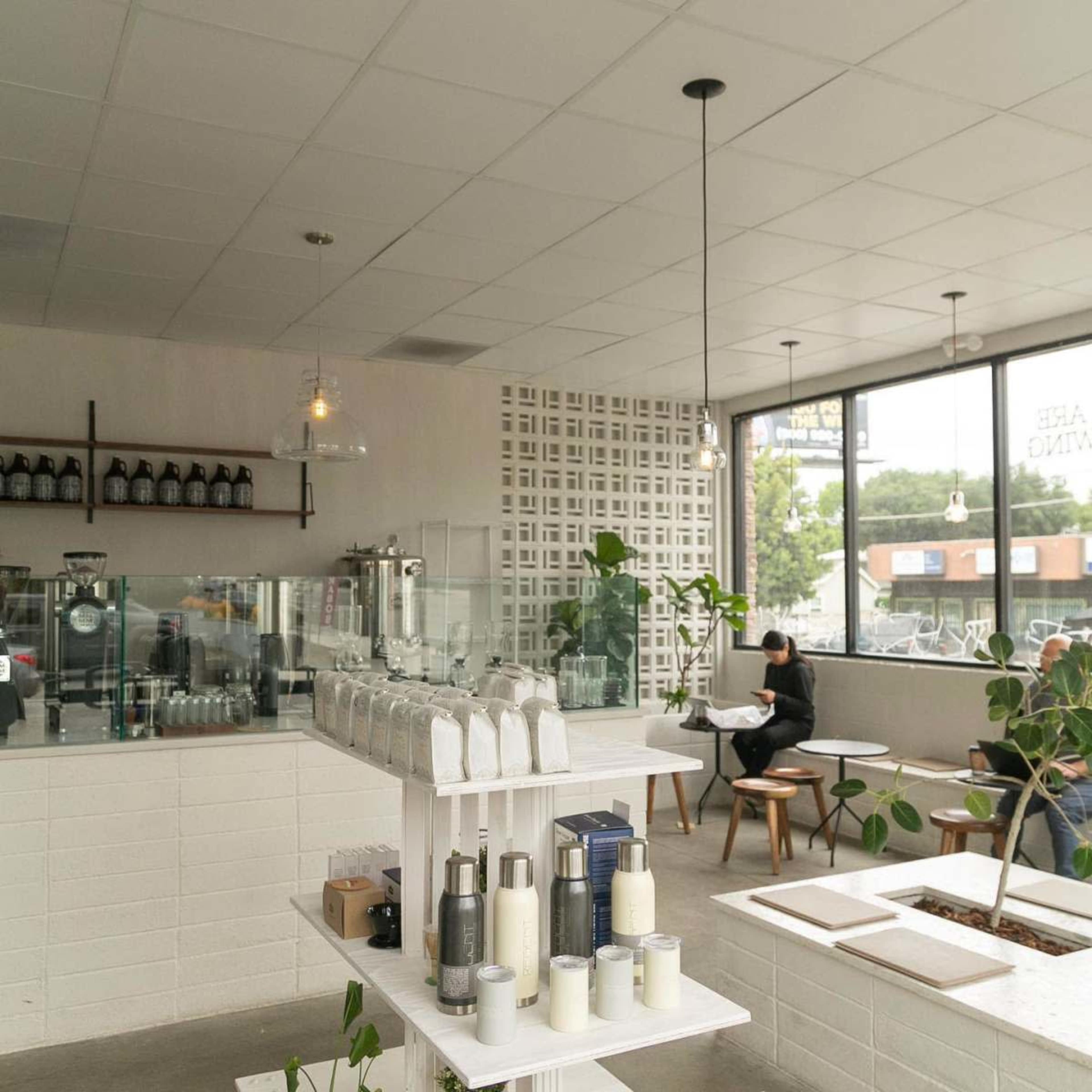 A modern cafe interior featuring a minimalist counter, a display of beverages, and seating areas with large windows letting in natural light.