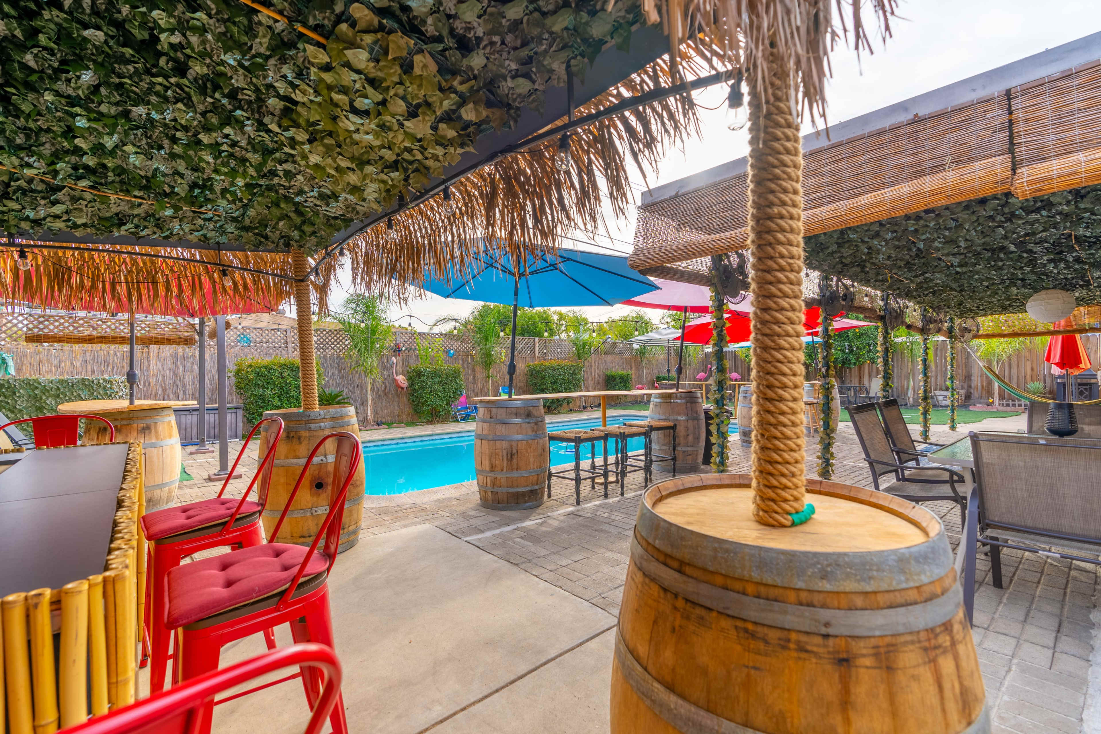 A poolside area with tropical-themed seating, a bar, and shaded umbrellas.