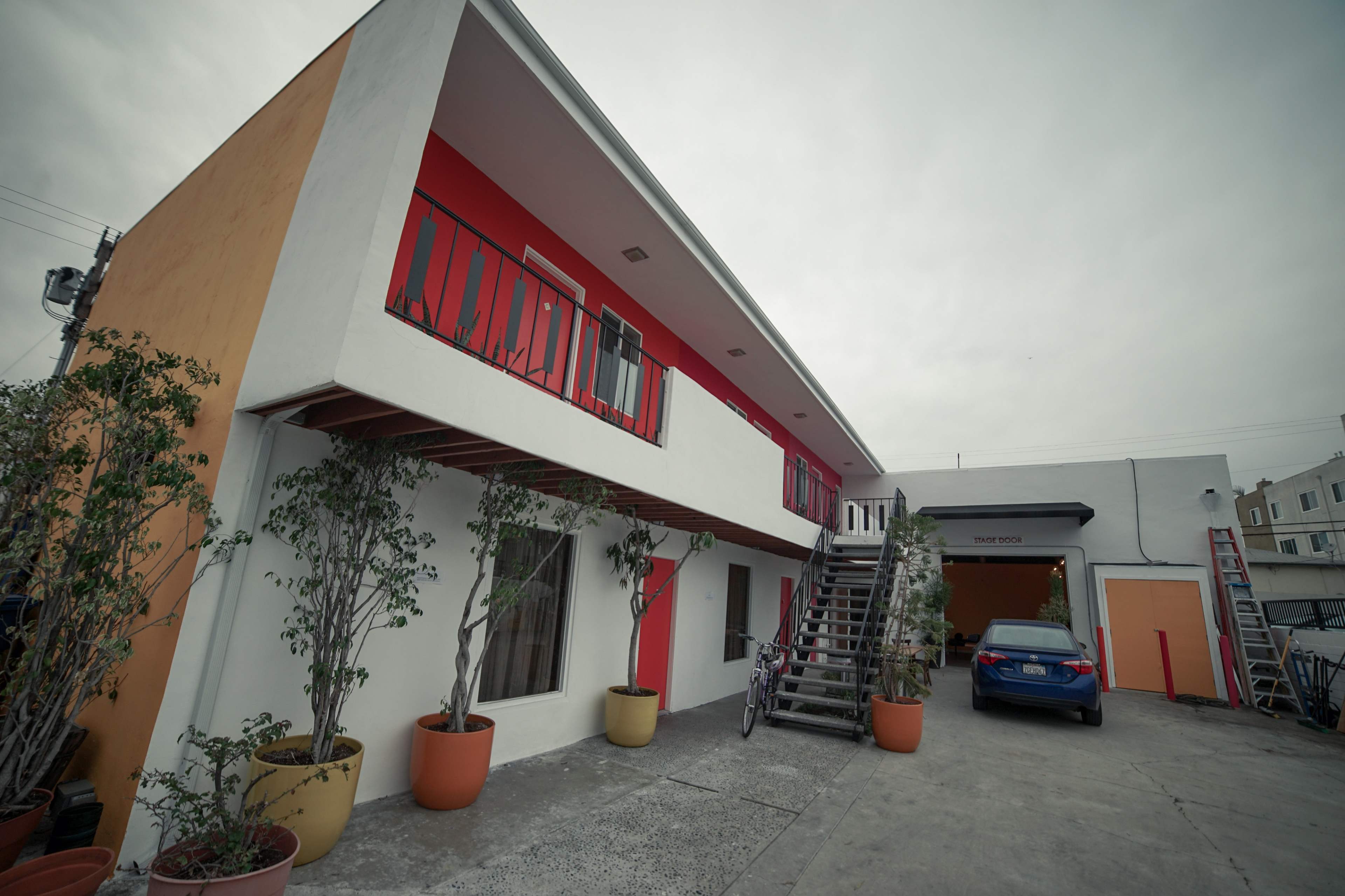 A two-story building with a red and white exterior, featuring potted plants and a staircase leading to the upper floor.