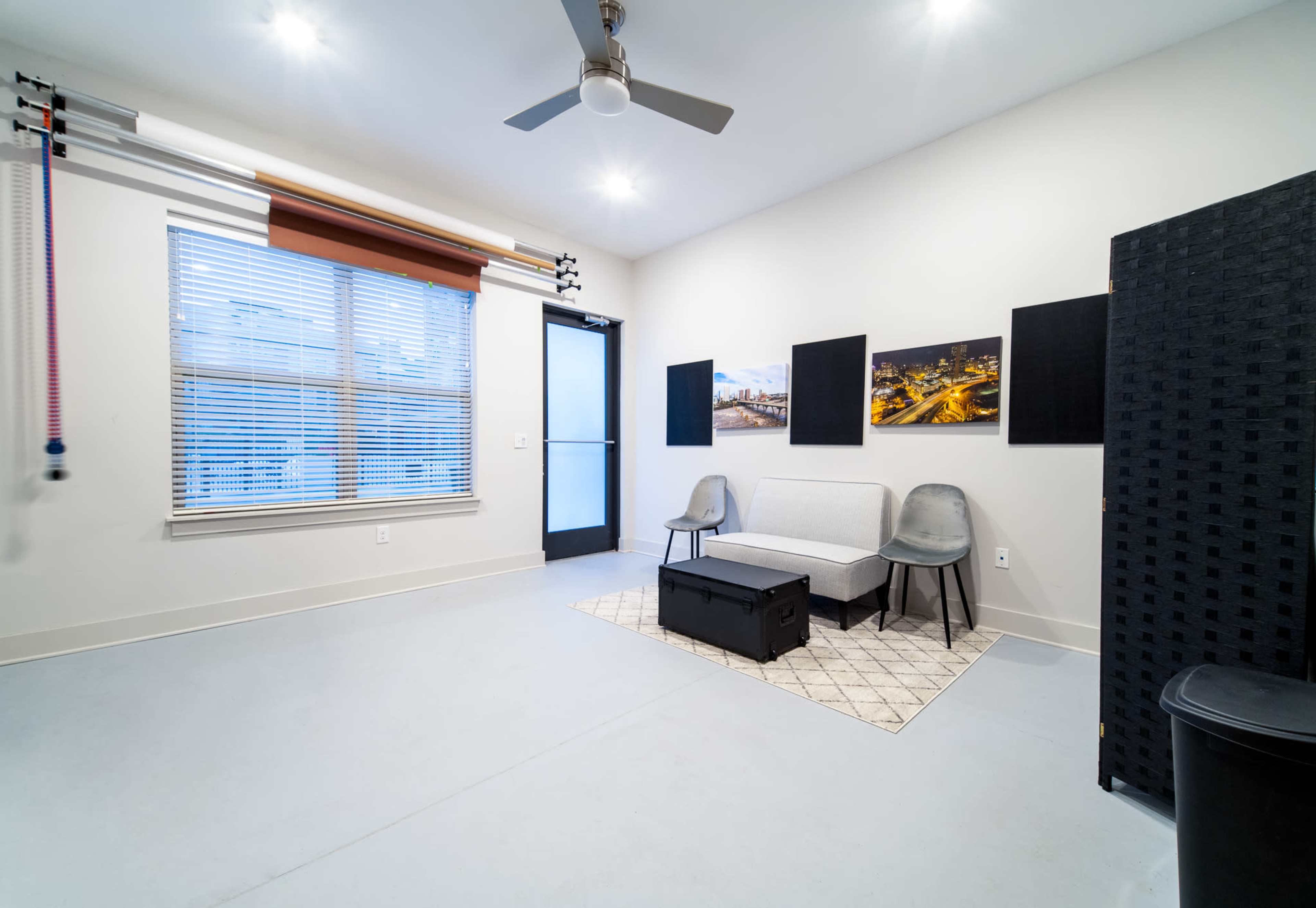 The image shows a minimalist interior room with a sofa, two chairs, and a coffee table, featuring large windows and modern decor.