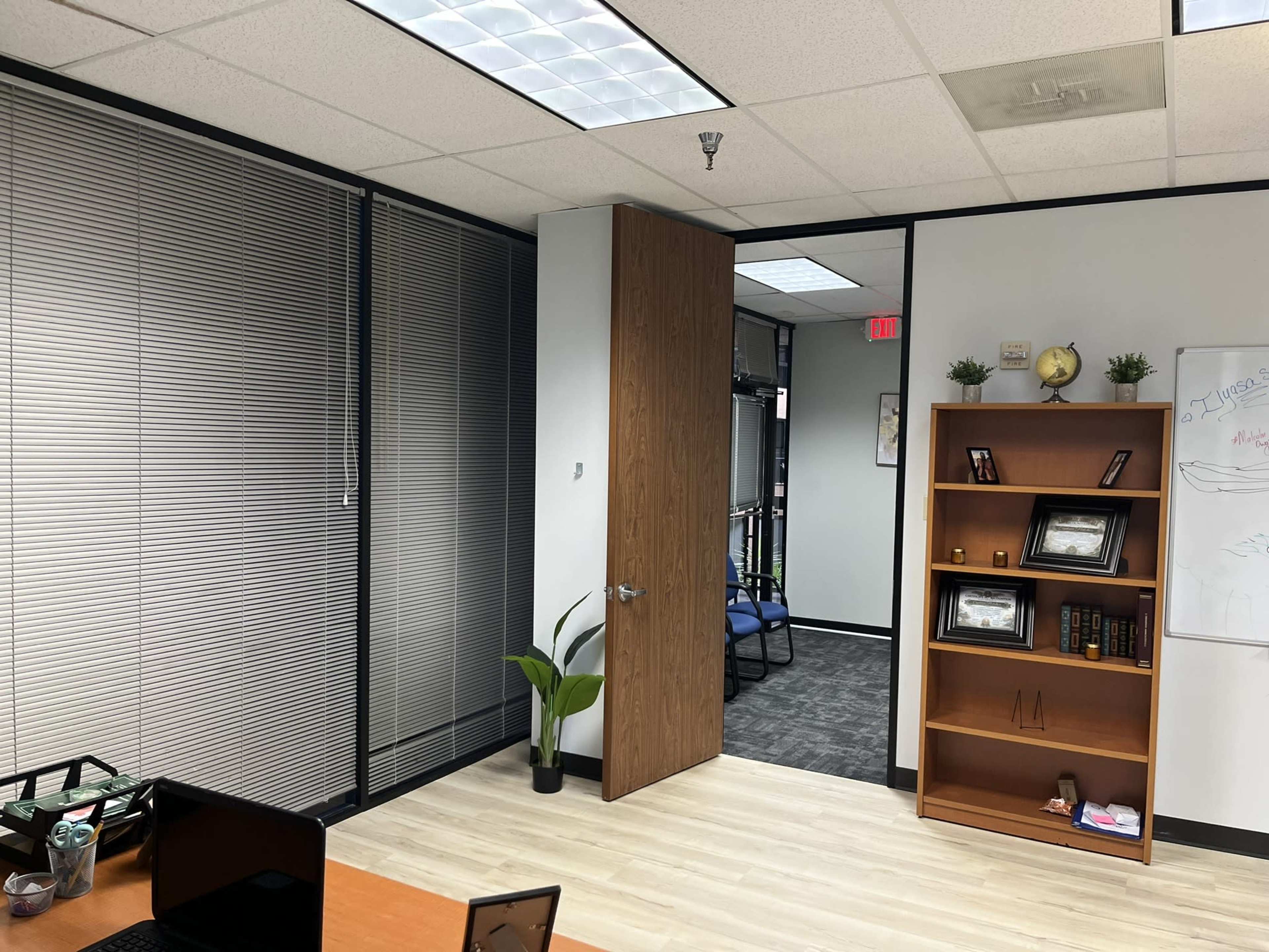 The image shows an office area featuring a door leading to another room, a bookshelf against the wall, and a desk with a laptop on it.