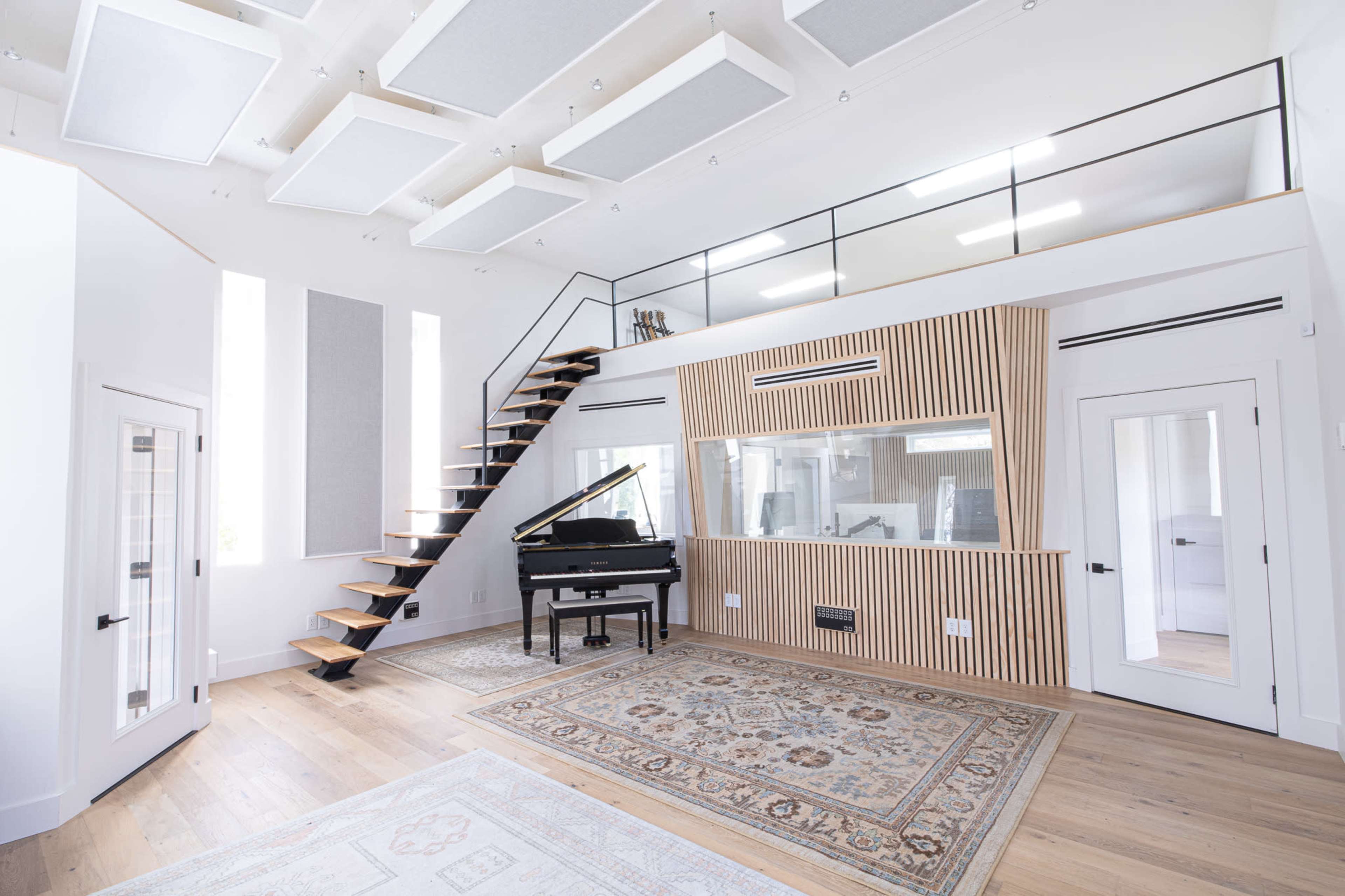 A modern music room featuring a grand piano, a staircase leading to a loft area, and soundproofing panels on the walls.