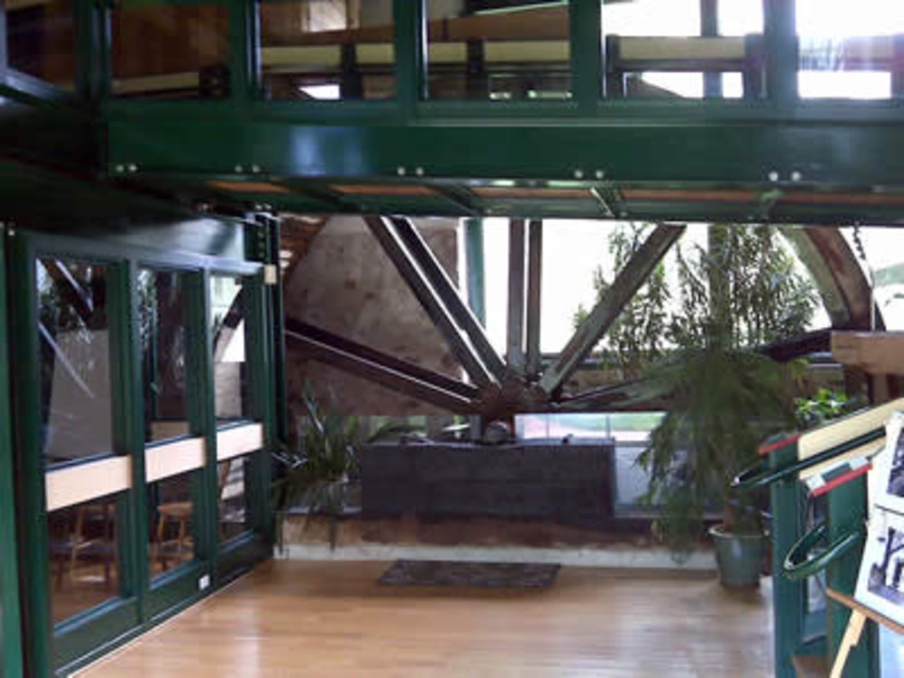 A modern interior space featuring a large, exposed wheel structure and greenery, with glass doors and wooden flooring.