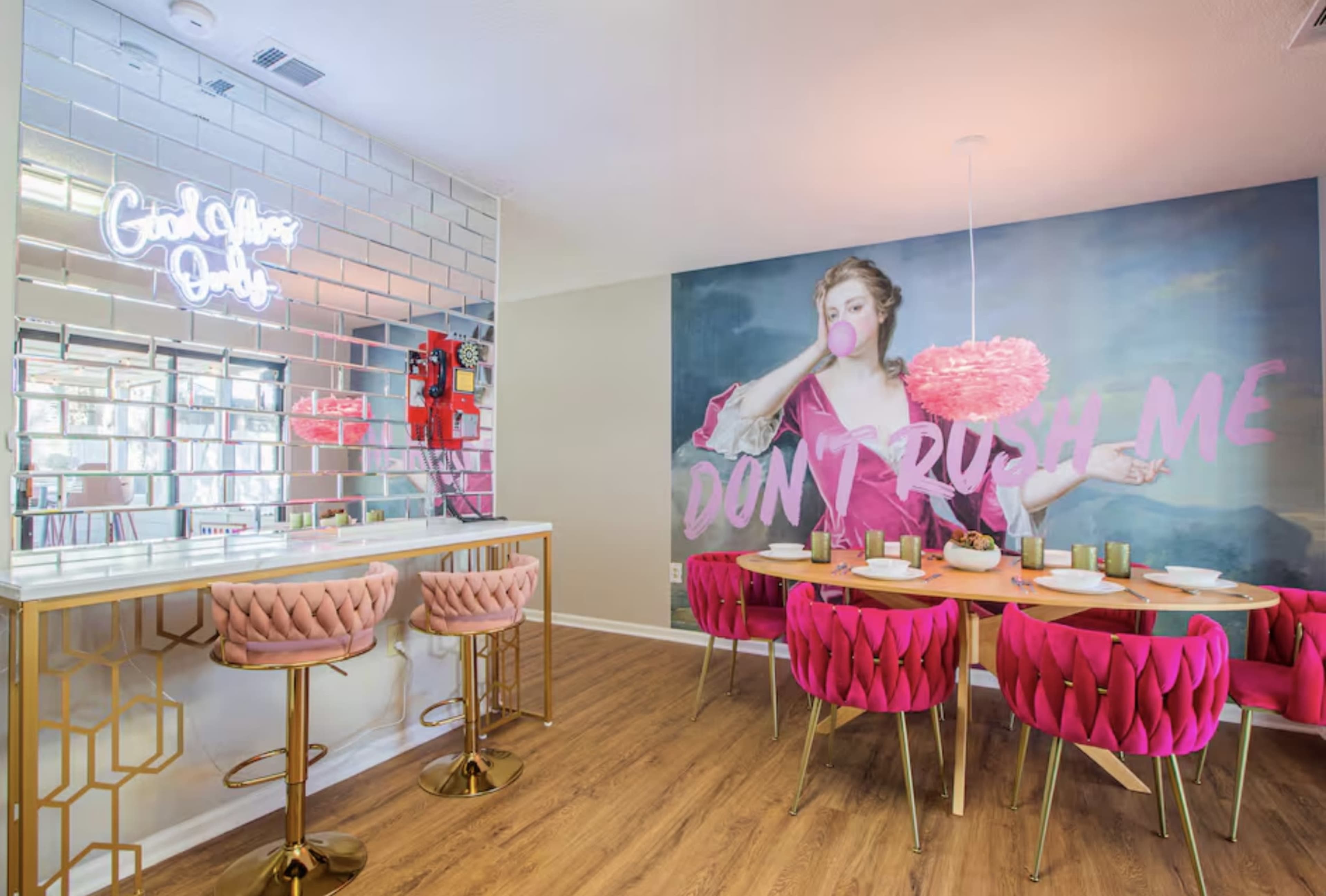 The image shows a modern dining area with a pink-themed decor, featuring a mirrored bar, round pink chairs, and a wall mural of a woman blowing a bubble with the text "DON'T RUSH ME."
