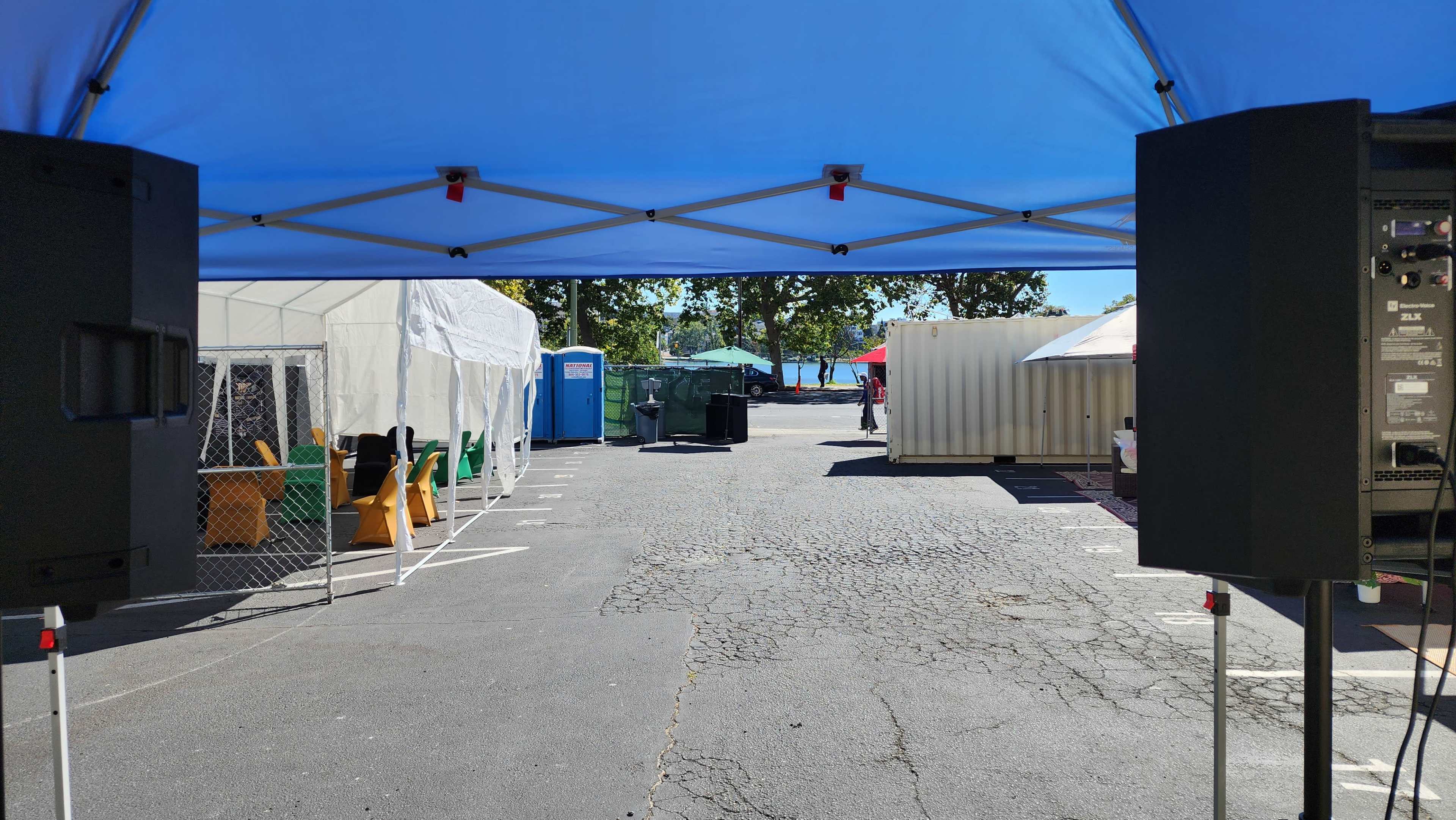 A view of a crowded outdoor event space with tents on either side, a portable restroom in the distance, and people moving around.