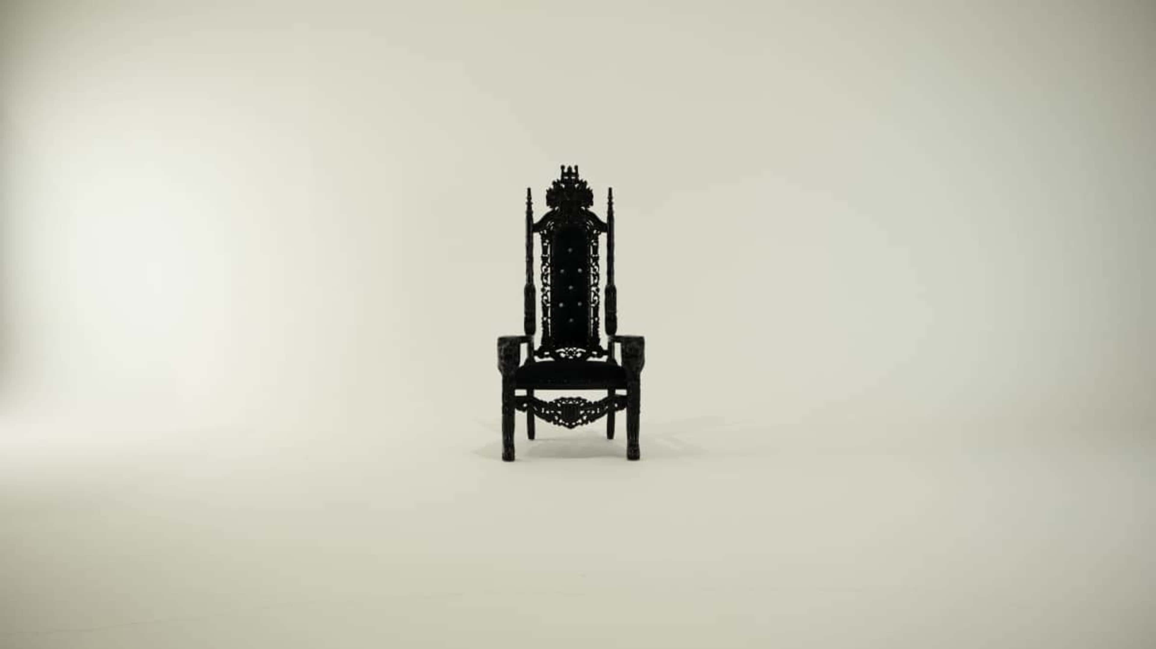 A large, intricately designed black throne is centered in an empty room with a plain white background.