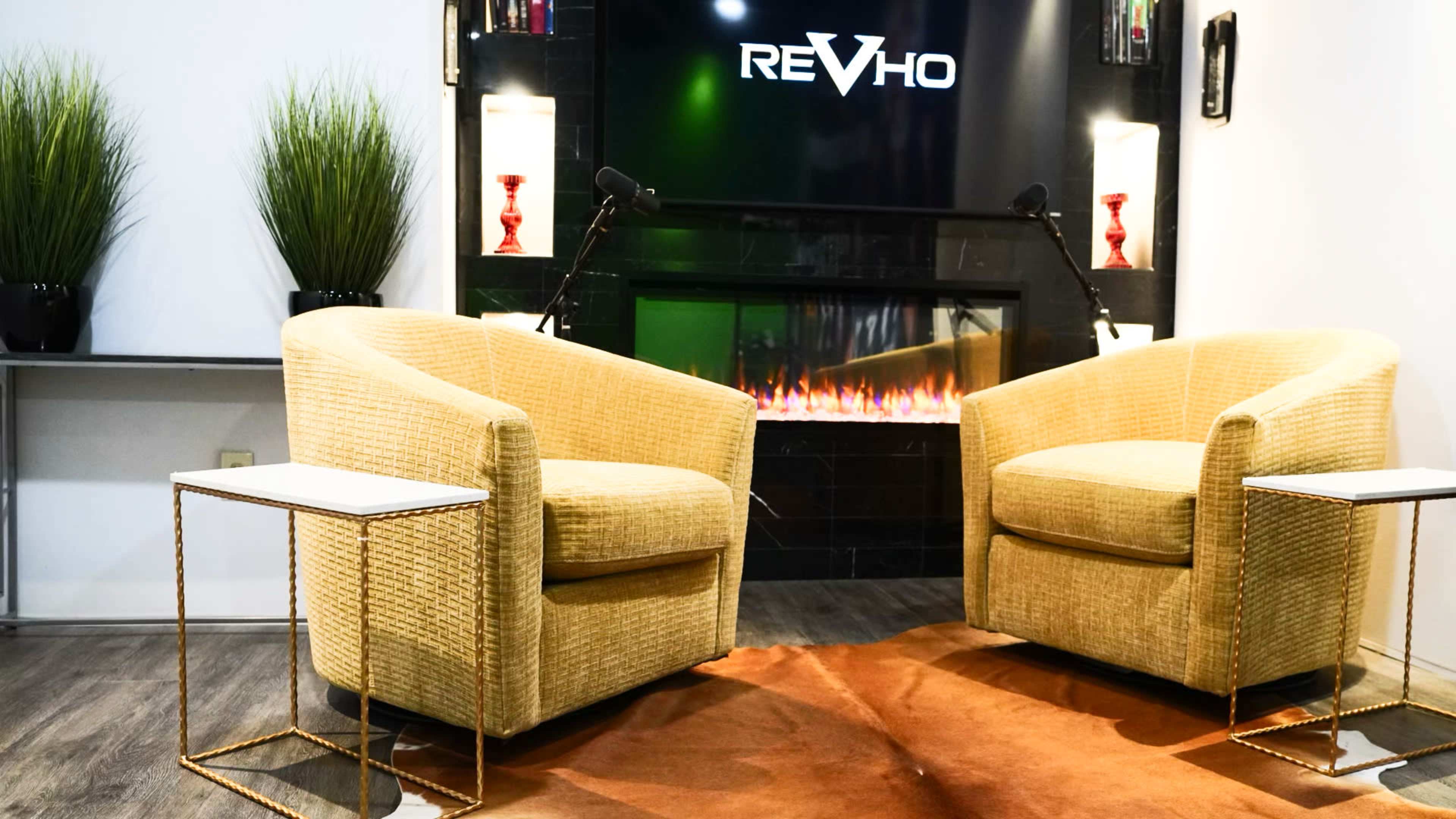 Two yellow chairs are positioned facing each other in a modern living space with a decorative fireplace and a sign that reads "REVHO."