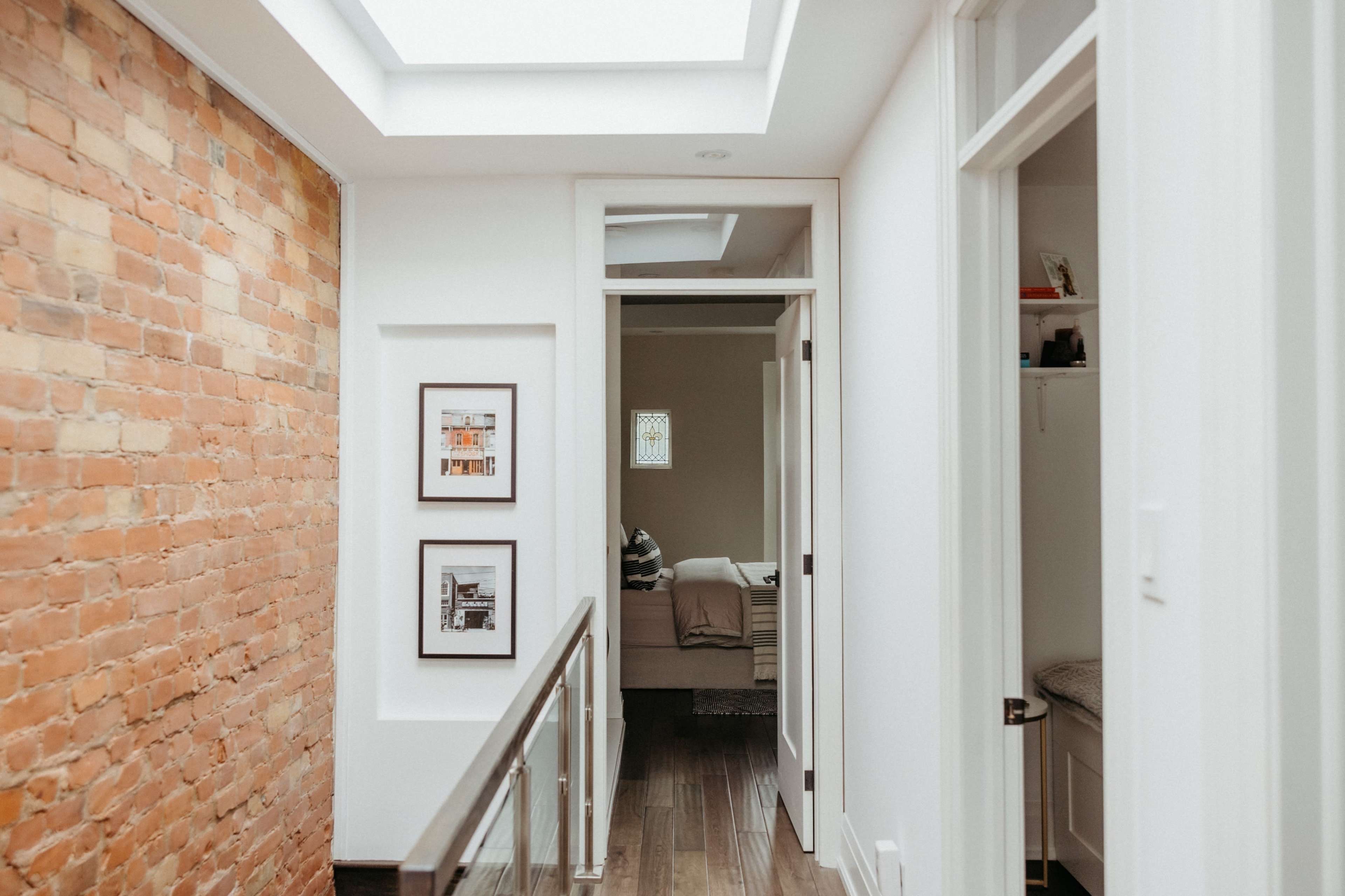 A hallway with exposed brick walls, framed pictures, and doors leading to a bedroom and a bathroom.