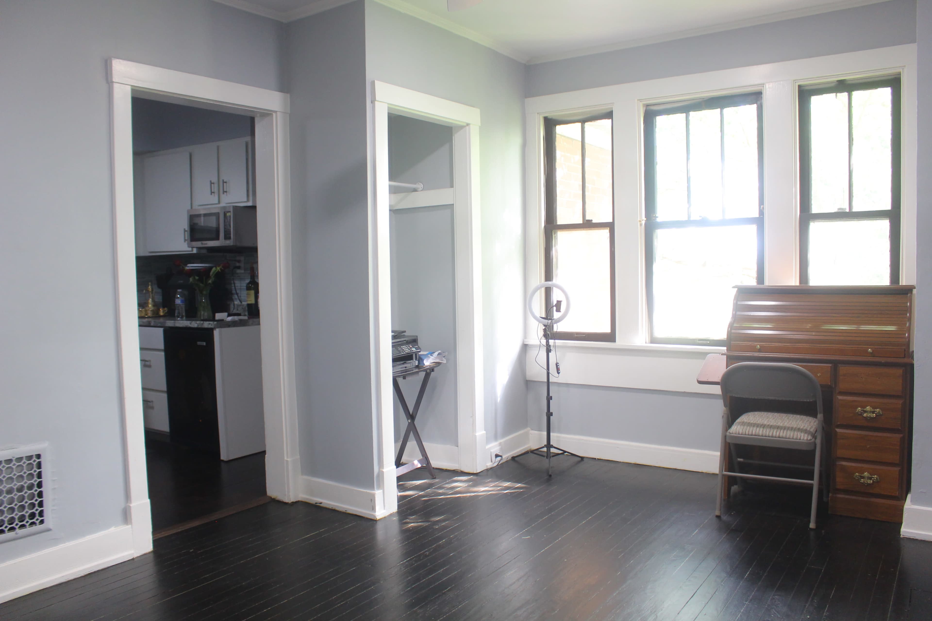 A room with light blue walls, featuring a desk with a chair, two windows, a door leading to another room, and a small folding table.
