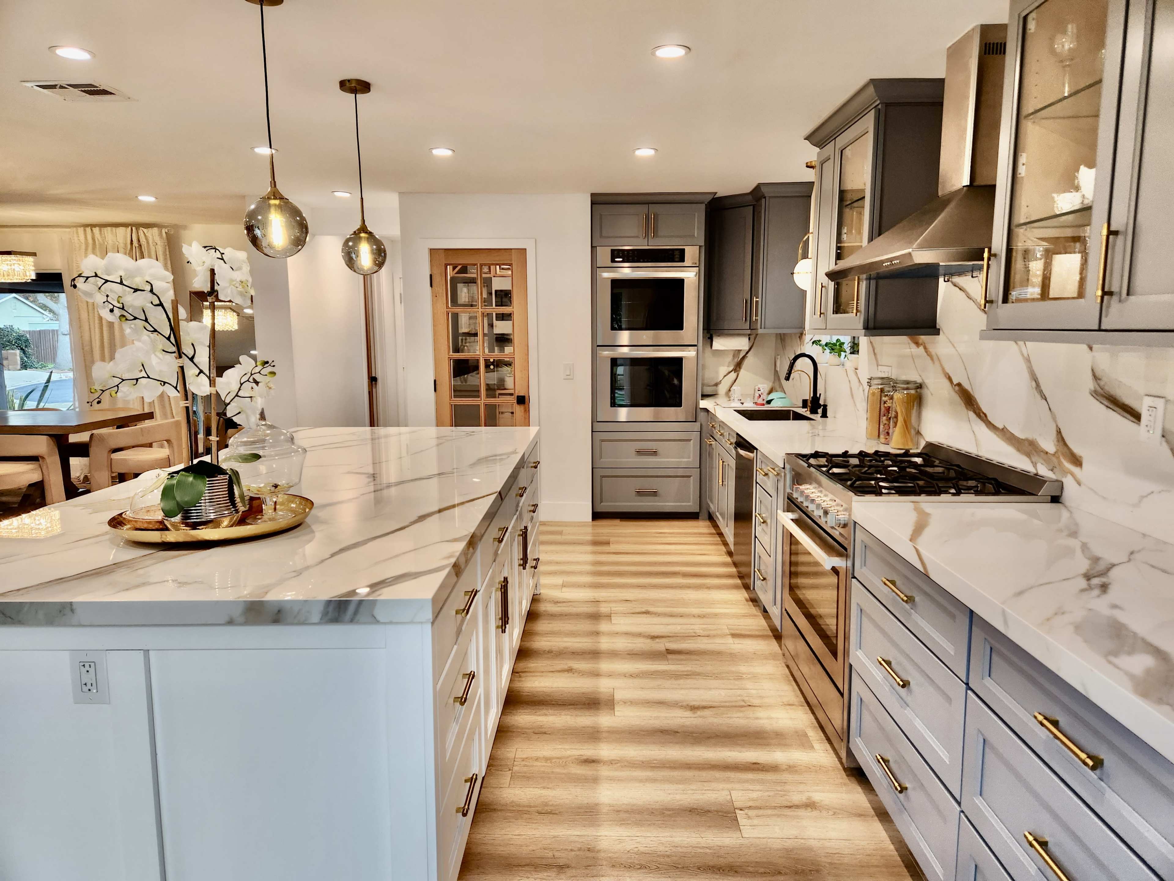 A modern kitchen with a large island, gray and white cabinetry, marble countertops, and stainless steel appliances.