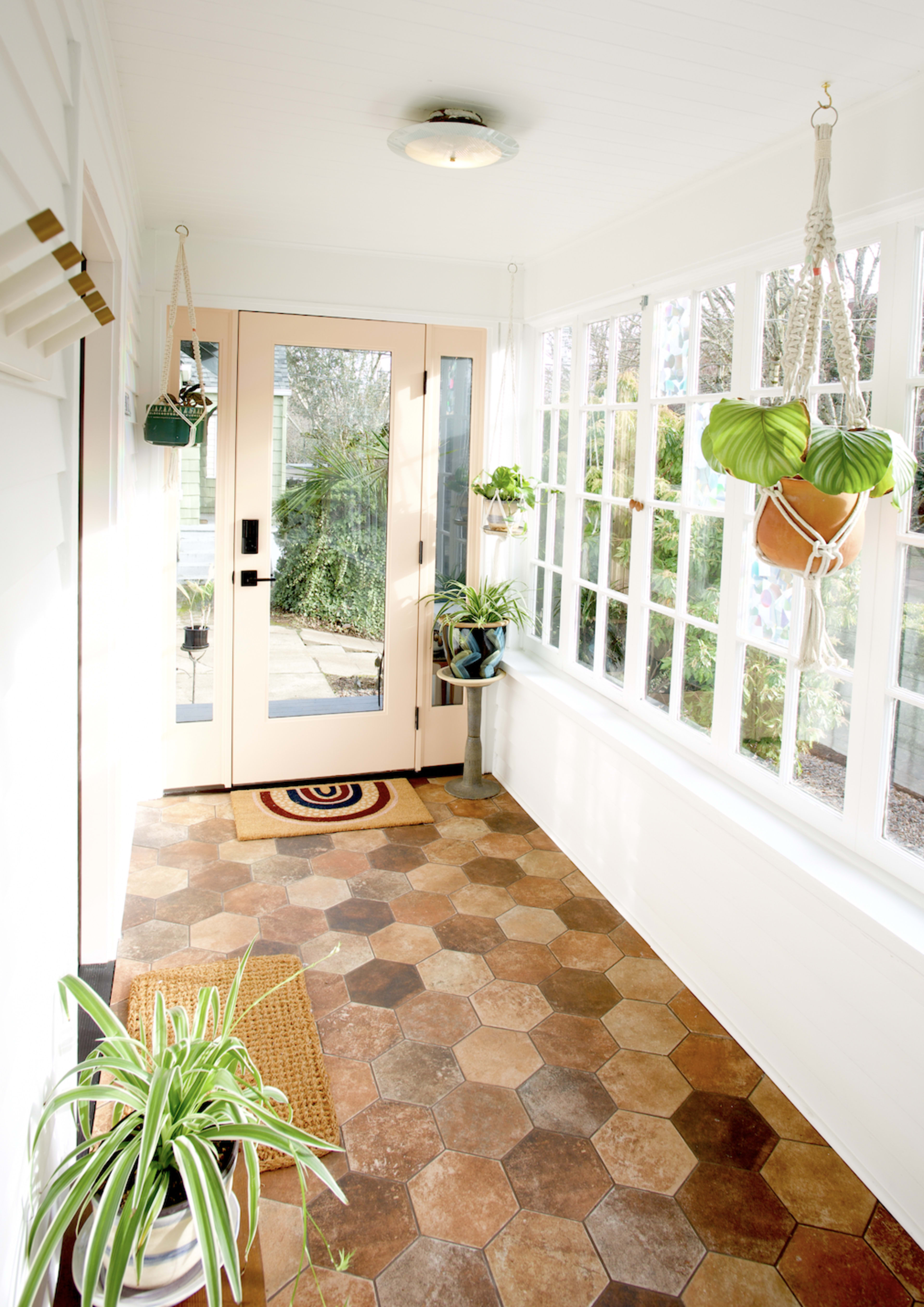 A bright sunroom with hexagonal tile flooring, hanging plants, and a door leading outside.